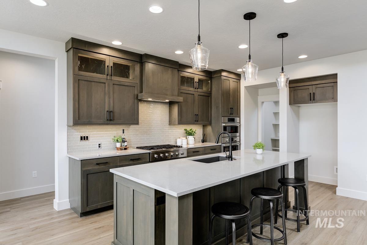 Kitchen with tasteful backsplash, decorative light fixtures, a breakfast bar area, recessed lighting, and glass insert cabinets