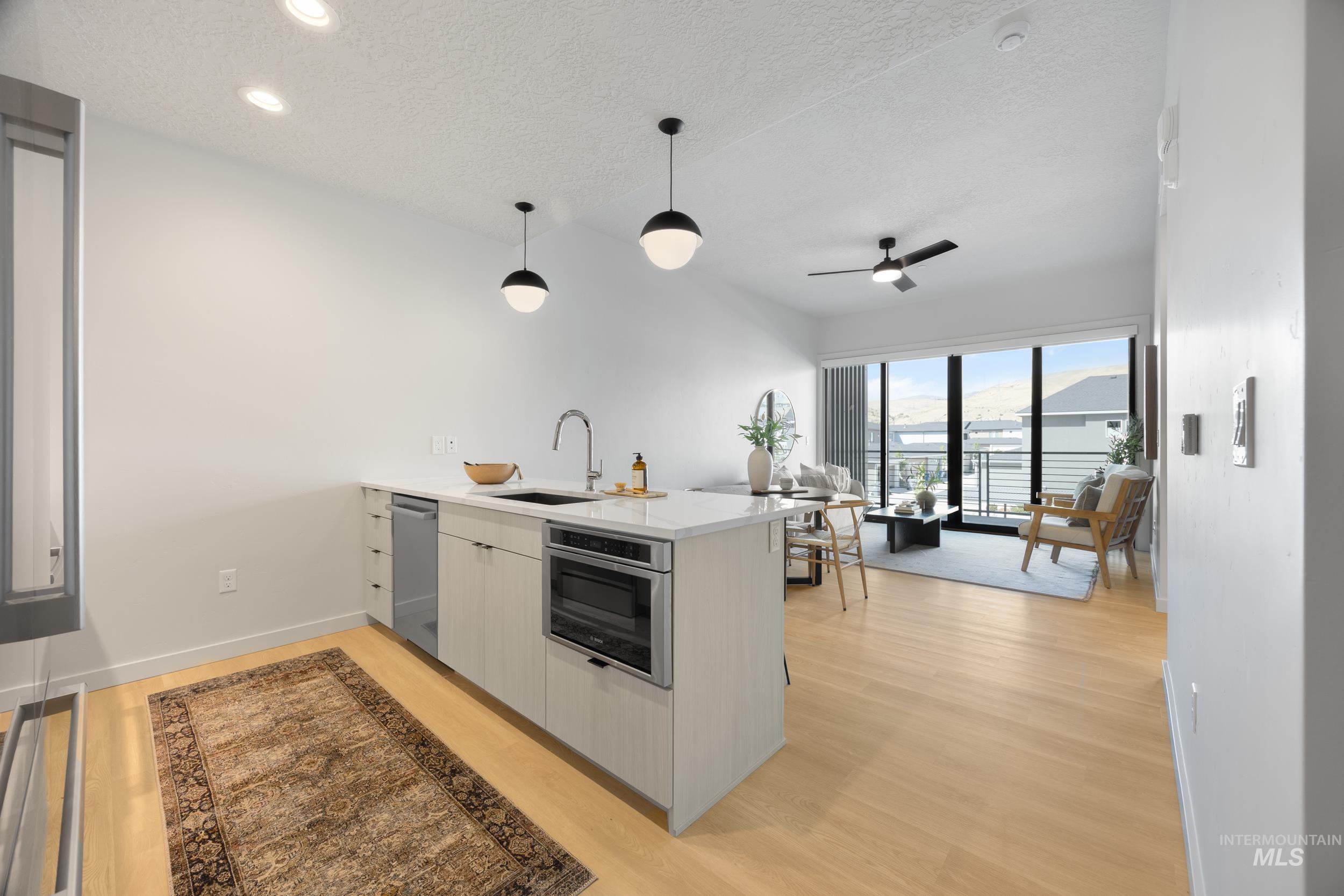 Kitchen with a peninsula, light wood-type flooring, a textured ceiling, decorative light fixtures, and light countertops