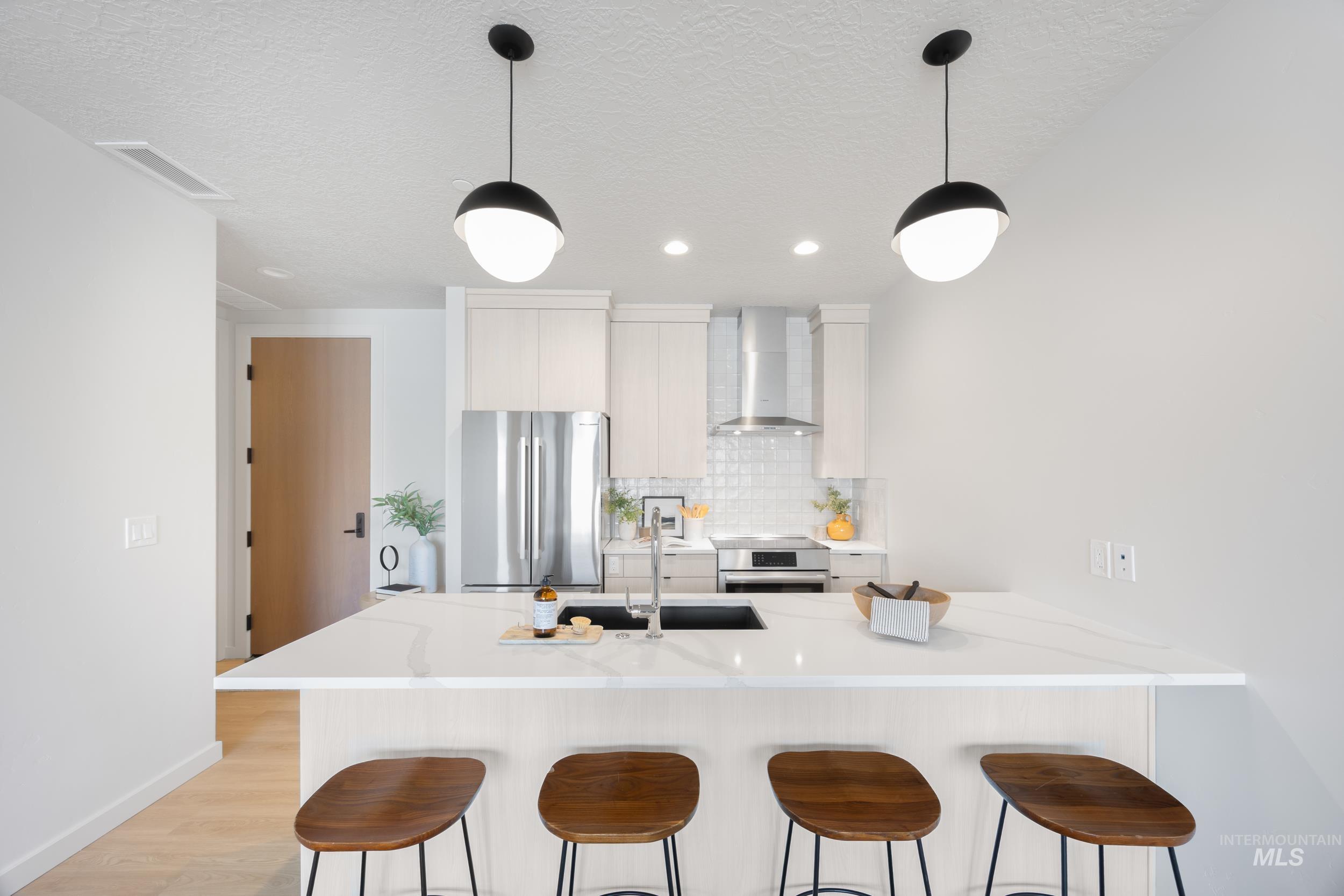 Kitchen with a kitchen bar, freestanding refrigerator, wall chimney range hood, decorative backsplash, and light countertops
