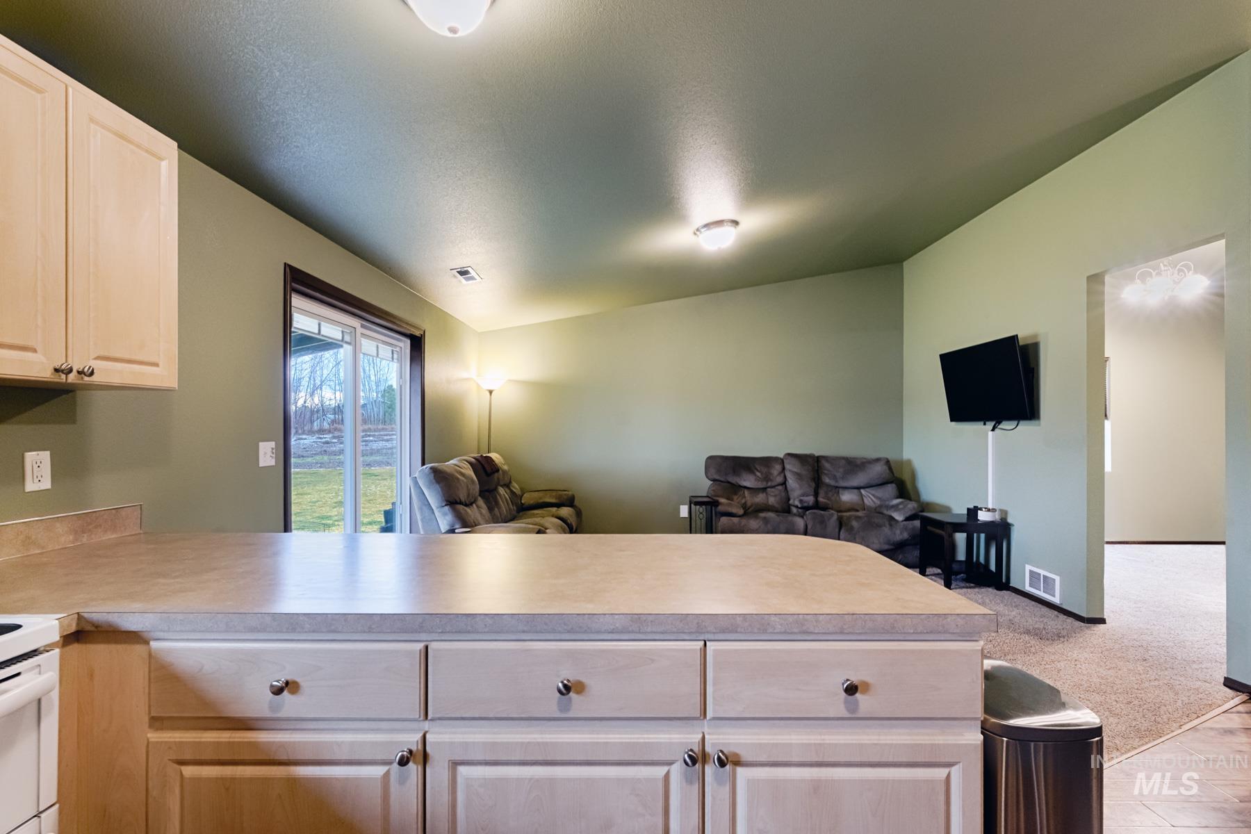 Kitchen with open floor plan, a peninsula, light countertops, lofted ceiling, and light wood finish cabinets