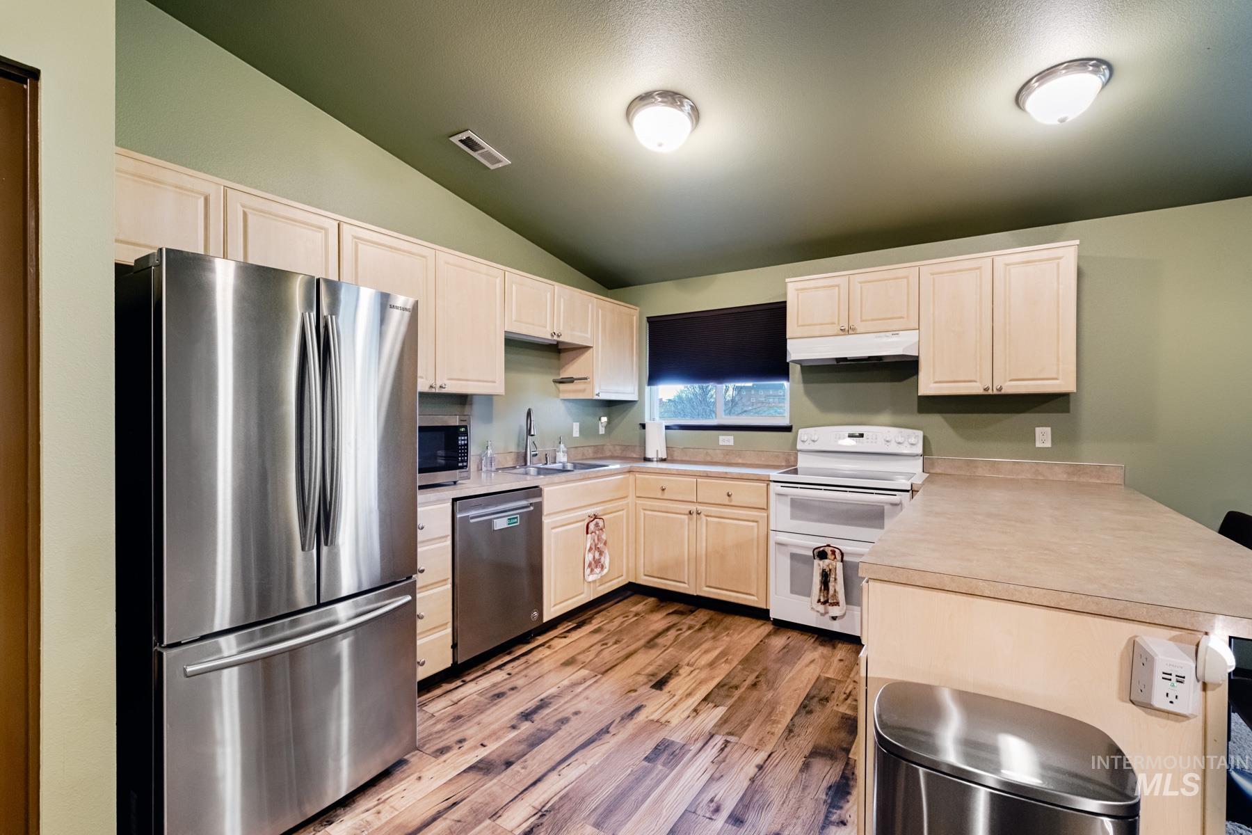 Kitchen featuring stainless steel appliances, lofted ceiling, light countertops, light wood finished floors, and light wood finish cabinets