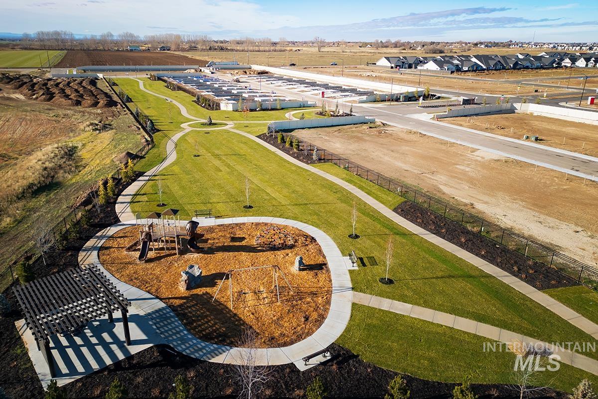 Community green space featuring a curved walking path, a children's play area with swings and a slide, an adjacent pergola, and mature landscaping