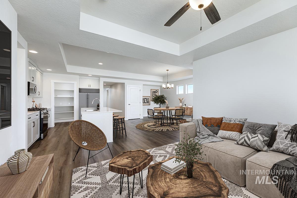 Spacious open-concept living area featuring wood-finish flooring, a contemporary kitchen with white cabinetry and stainless steel appliances, and a dining area with a modern chandelier