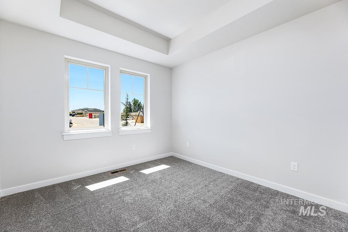 Bright interior space featuring two large windows, a tray ceiling, and new gray carpet