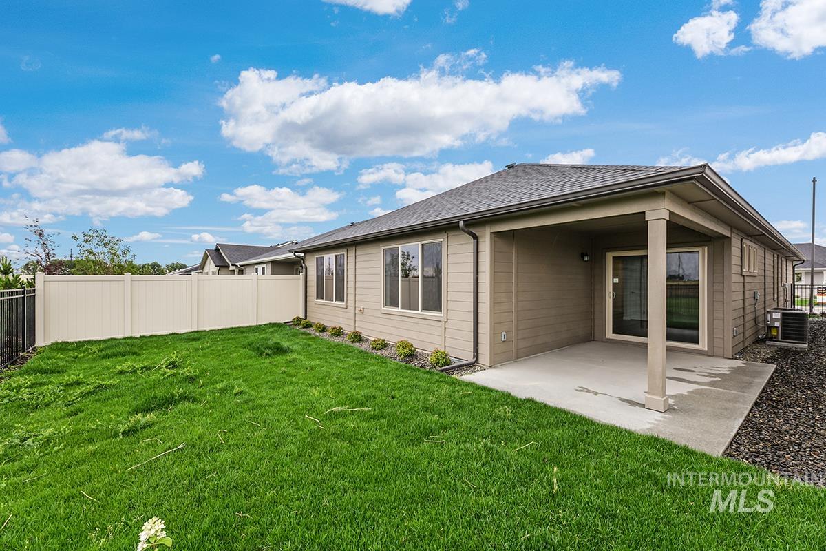 Expansive backyard featuring a covered concrete patio, sliding glass door access, vinyl fencing, and a manicured lawn