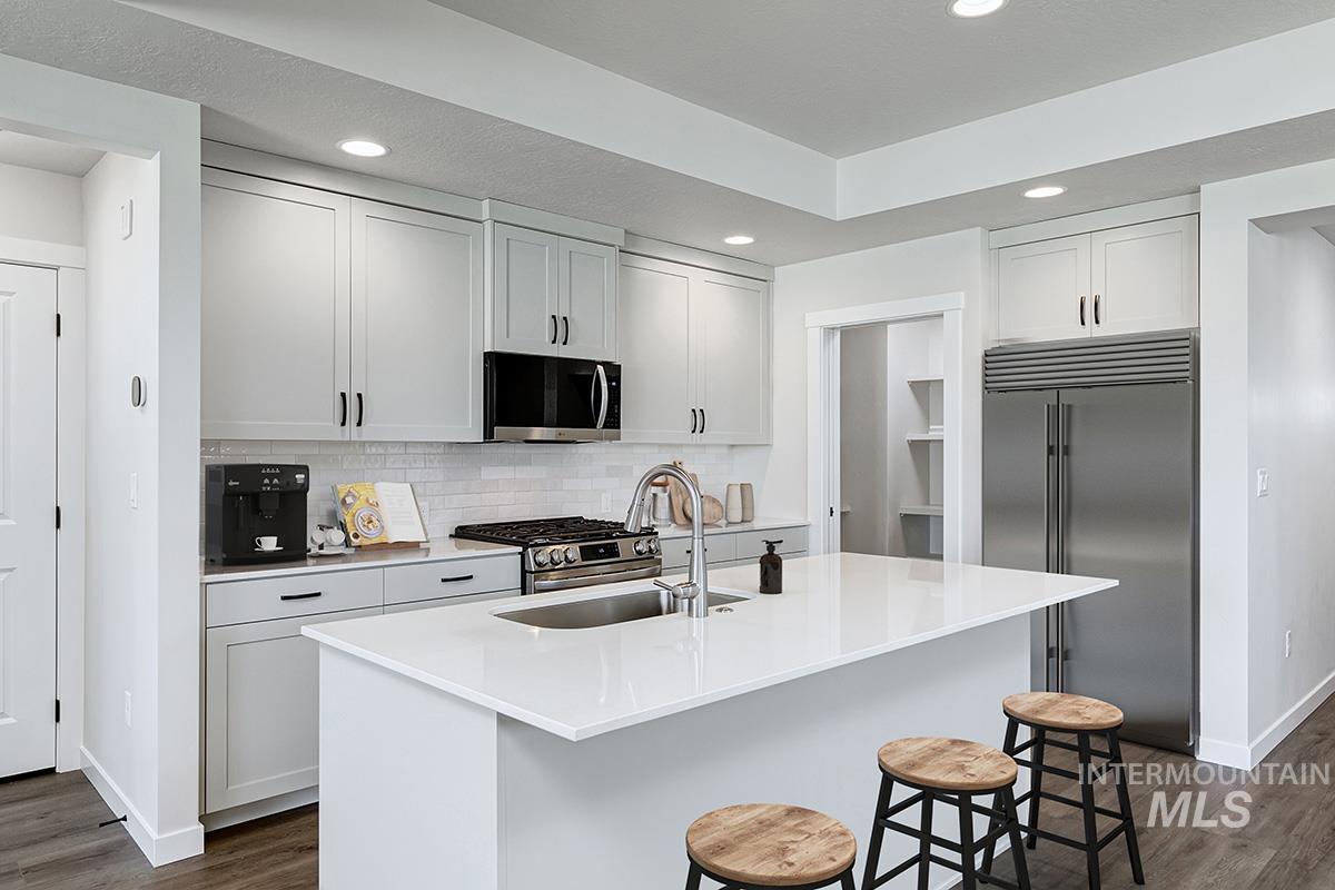 Modern kitchen featuring a large center island with integrated sink, stainless steel appliances, light gray shaker cabinetry, a white subway tile backsplash, and recessed lighting