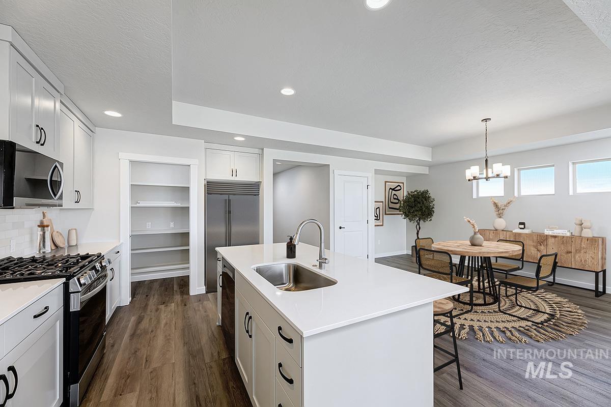 Open-concept kitchen and dining area featuring a spacious island with an undermount sink, white cabinetry, stainless steel appliances, and wood-finish flooring