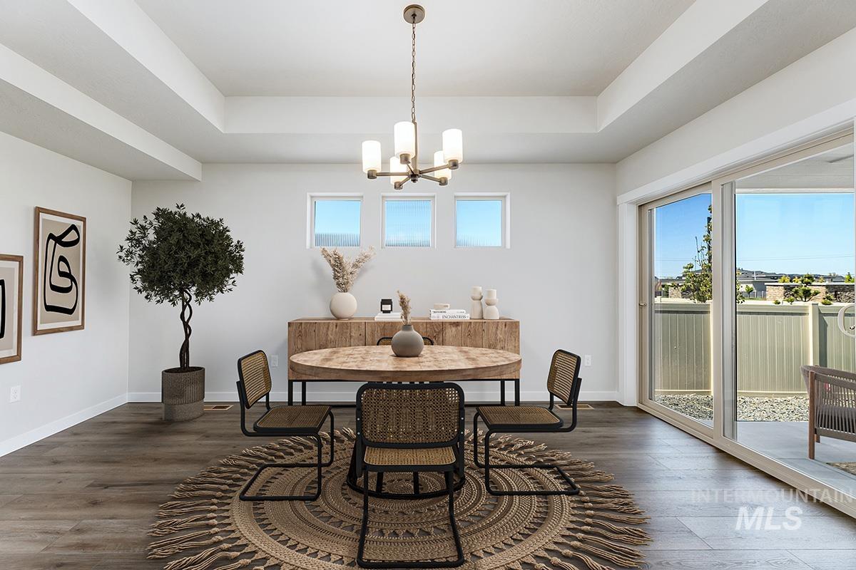 Spacious dining area featuring a tray ceiling, wood-finish flooring, and a modern chandelier