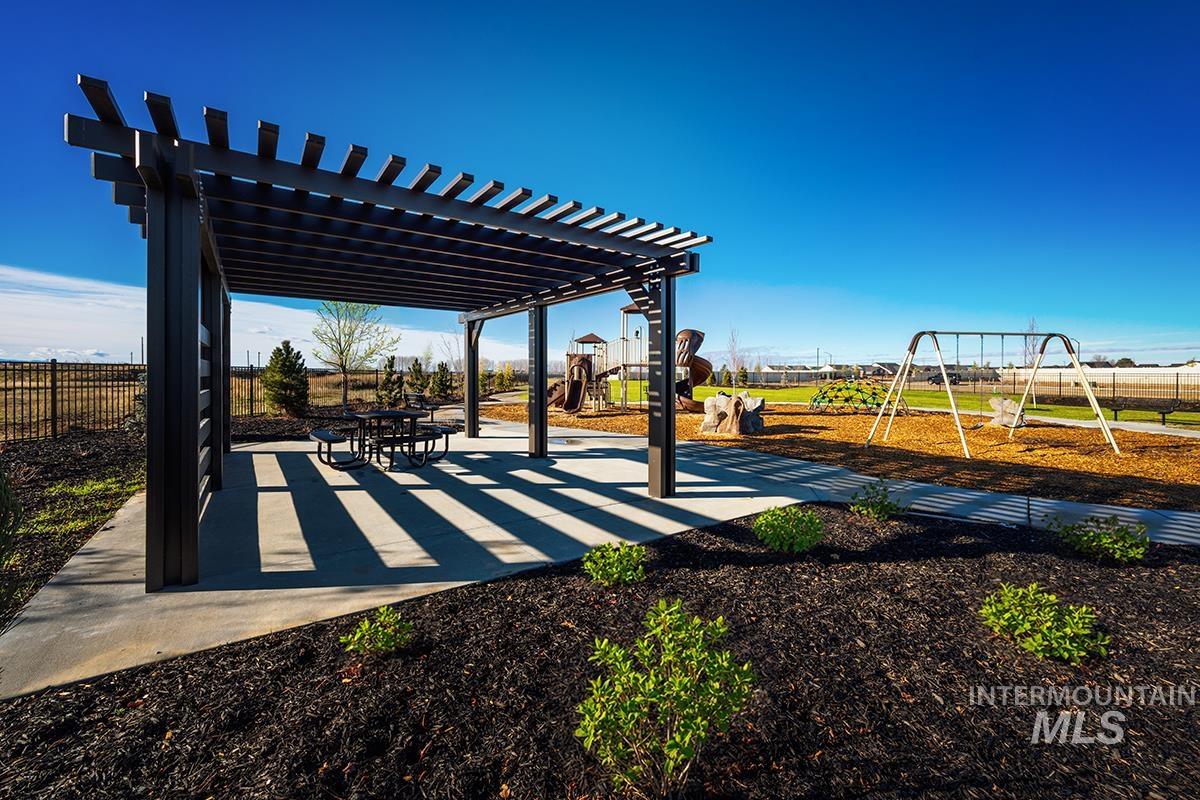 Expansive outdoor recreation area featuring a modern pergola with a built-in picnic table, a swing set, and a playground structure