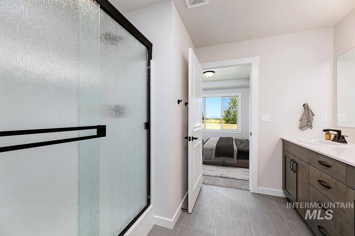 Frosted glass shower enclosure with black framing, wood-finish vanity with countertop, rectangular sink, and dark hardware