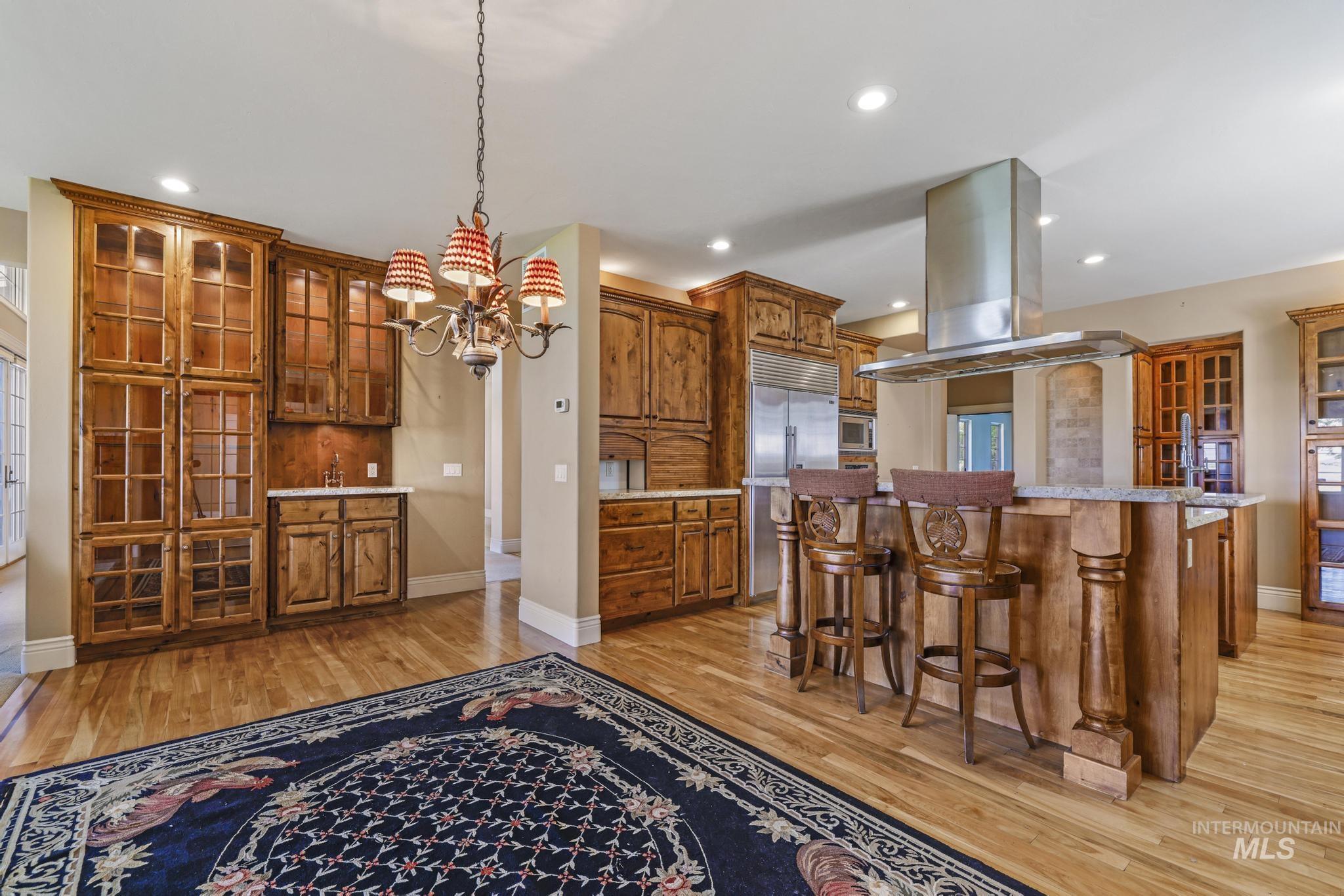 Kitchen featuring brown cabinets, a kitchen breakfast bar, island exhaust hood, glass insert cabinets, and light wood-type flooring
