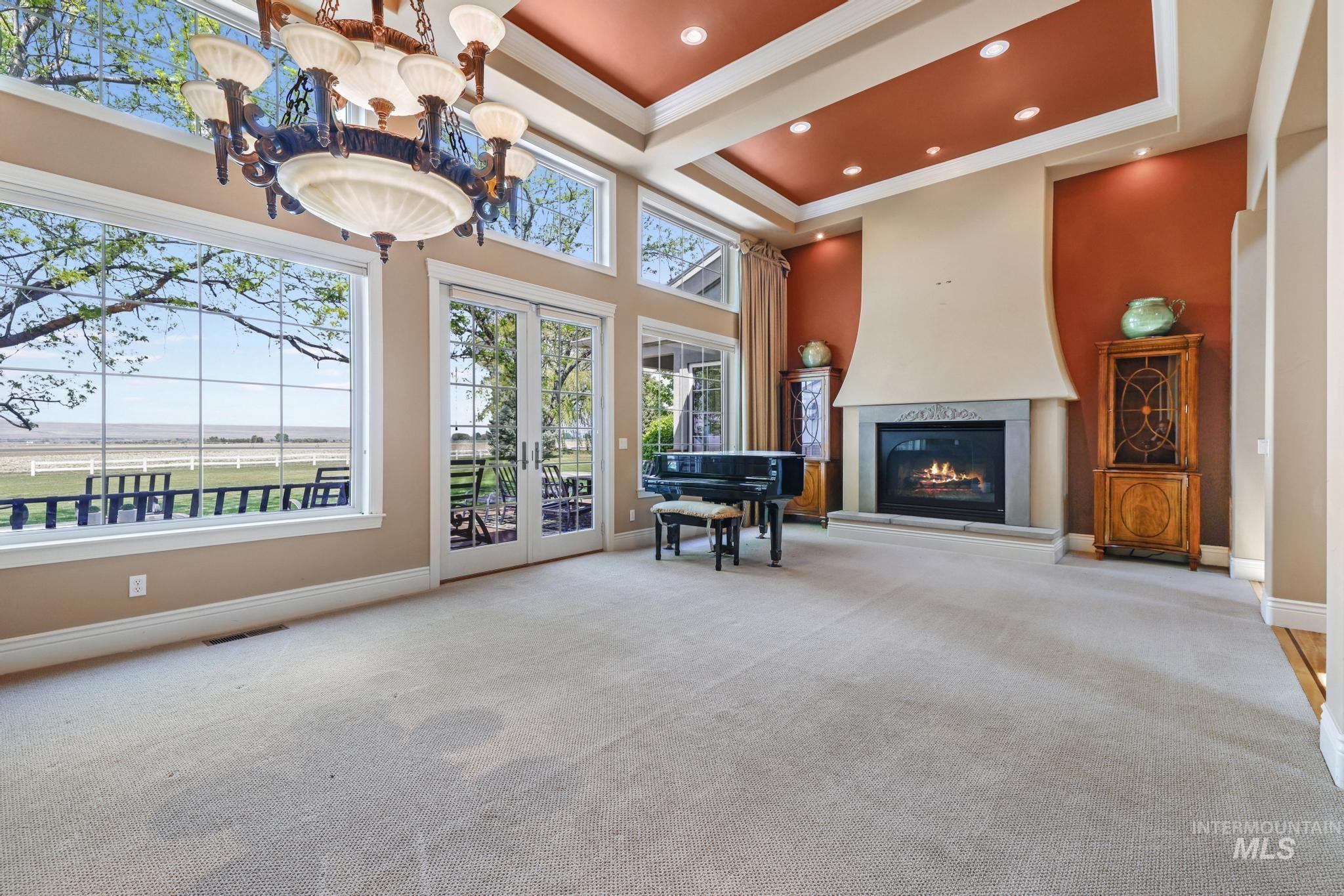 Living area featuring a tray ceiling, french doors, carpet, a glass covered fireplace, and crown molding