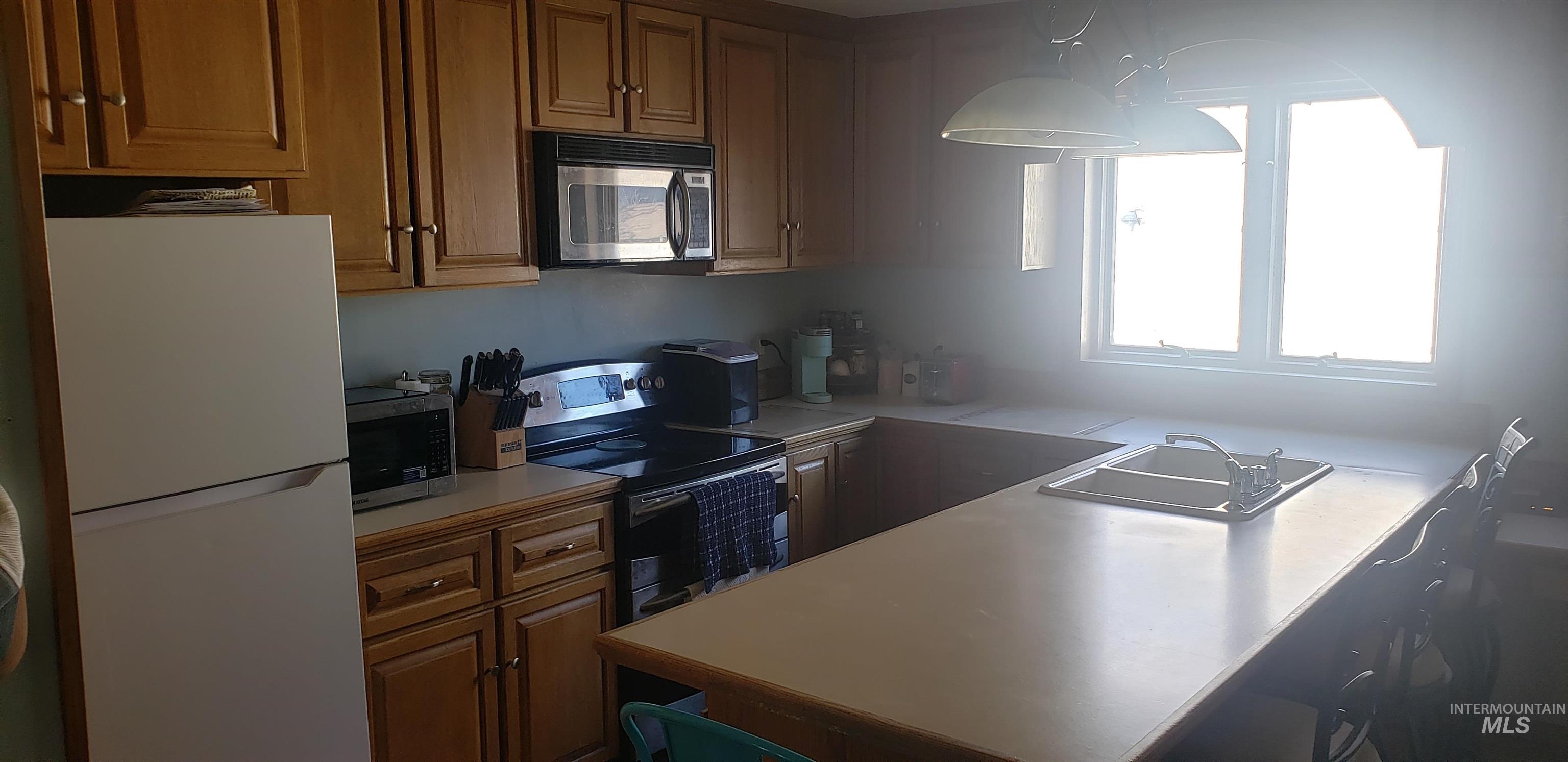 Kitchen with appliances with stainless steel finishes, light countertops, brown cabinets, and decorative light fixtures