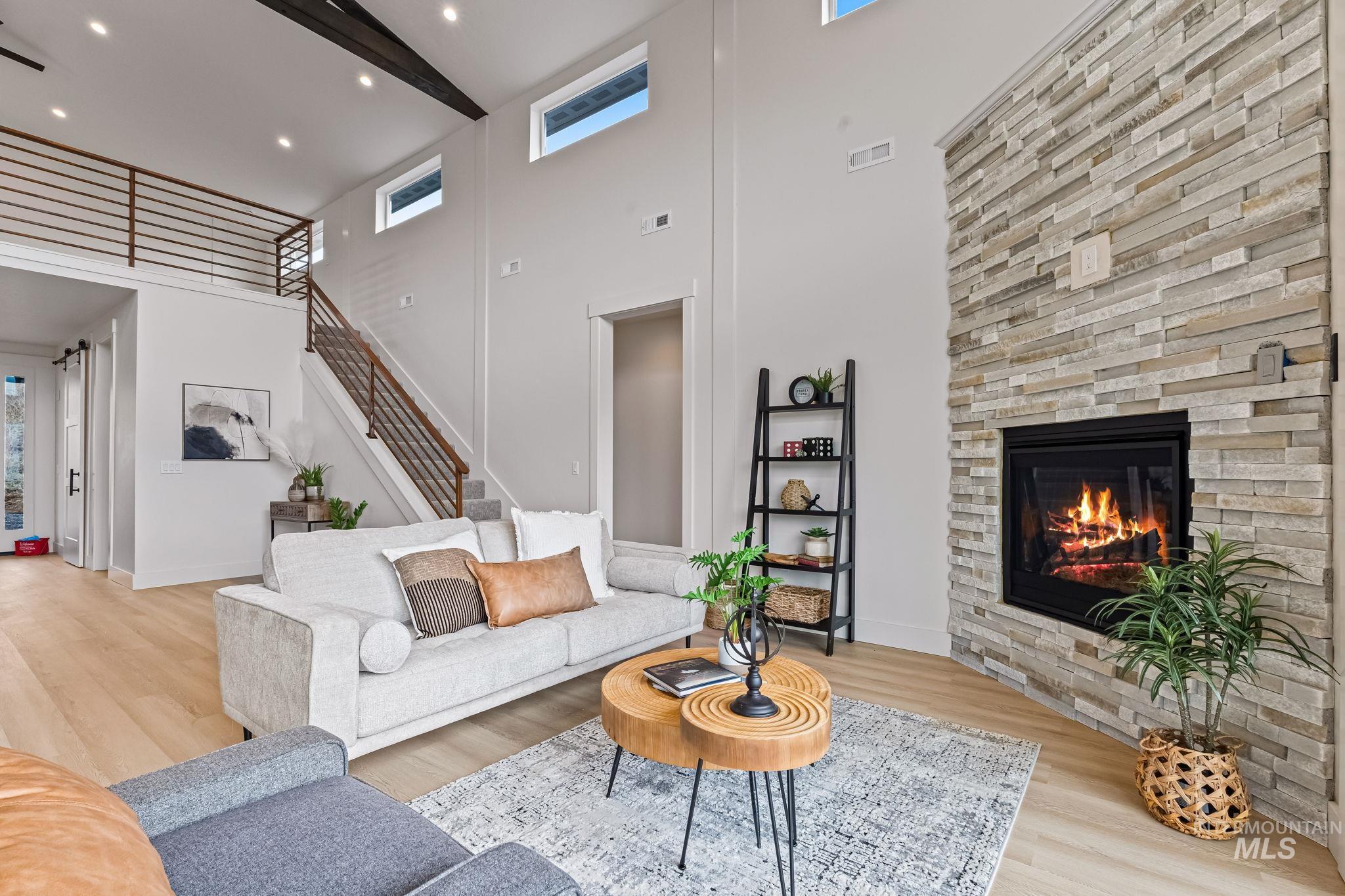Living room featuring light wood finished floors, a high ceiling, a stone fireplace, stairway, and recessed lighting