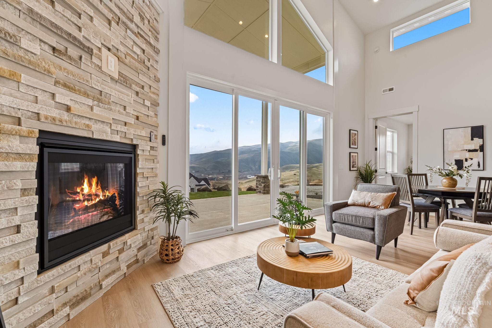 Living room with a mountain view, wood finished floors, a towering ceiling, a stone fireplace, and healthy amount of natural light