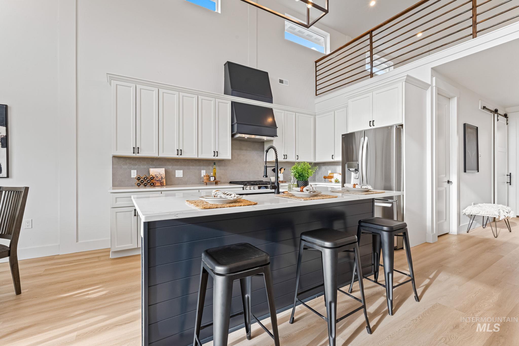 Kitchen with a towering ceiling, white cabinets, a breakfast bar area, and an island with sink