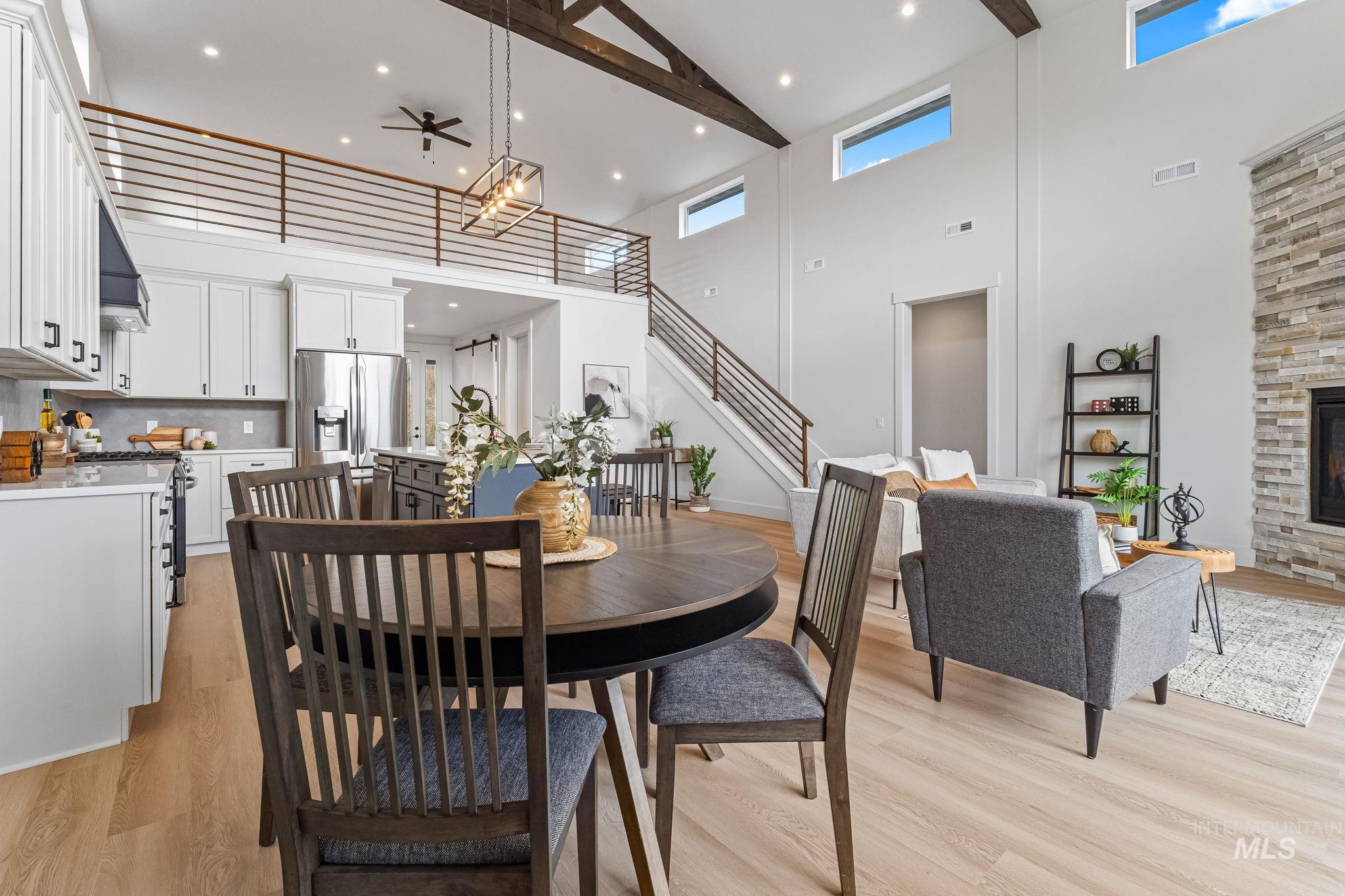 Dining area featuring stairs, a stone fireplace, light wood-type flooring, a towering ceiling, and ceiling fan