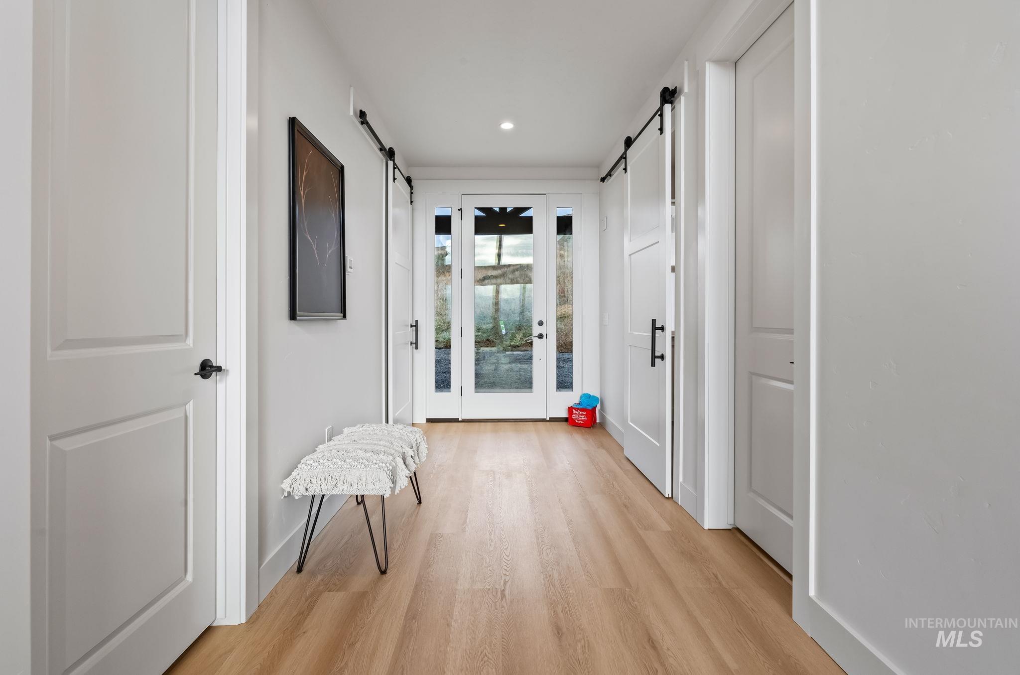 Corridor with a barn door, light wood-type flooring, and recessed lighting
