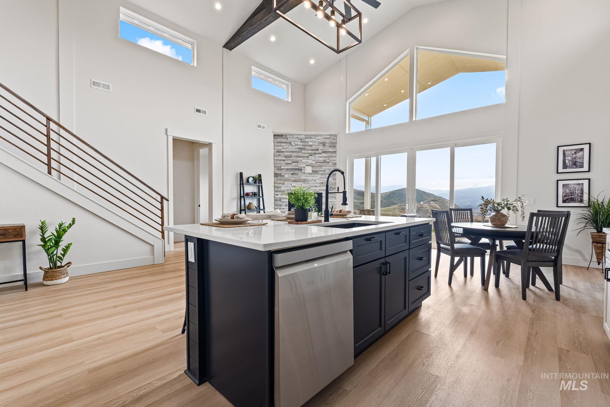 Kitchen featuring a kitchen island with sink, dishwasher, light stone countertops, dark cabinets, and high vaulted ceiling