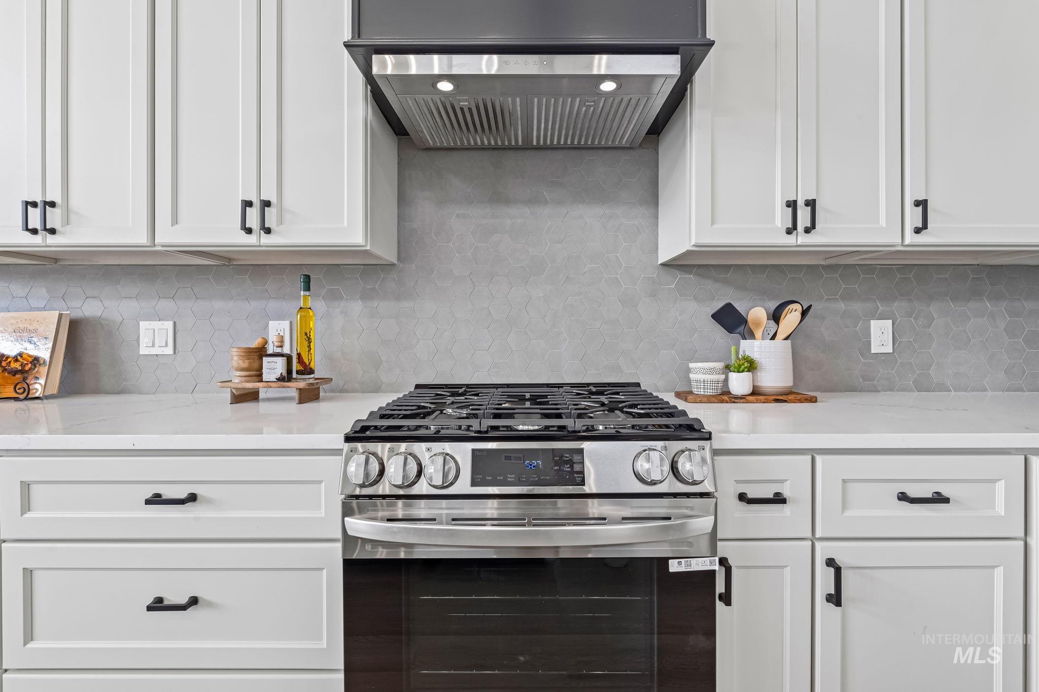 Kitchen featuring gas stove, under cabinet range hood, white cabinets, and light stone counters