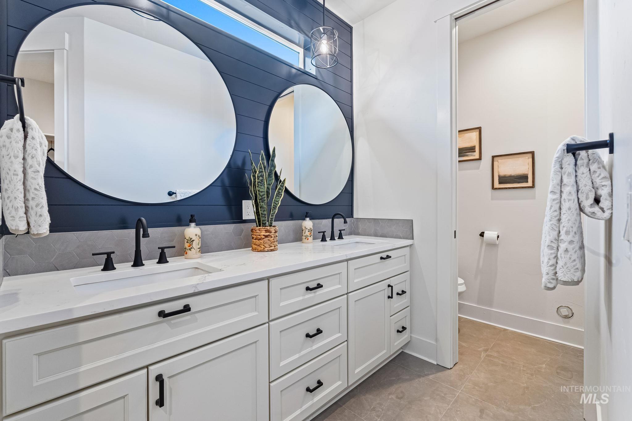 Bathroom featuring double vanity, light tile patterned floors, and decorative backsplash