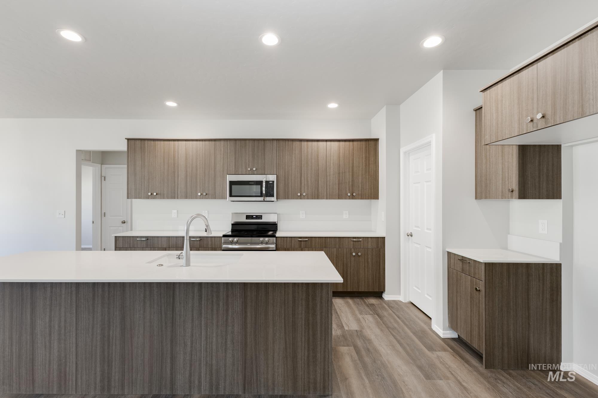 Kitchen featuring stainless steel appliances, light countertops, wood finished floors, recessed lighting, and modern cabinets