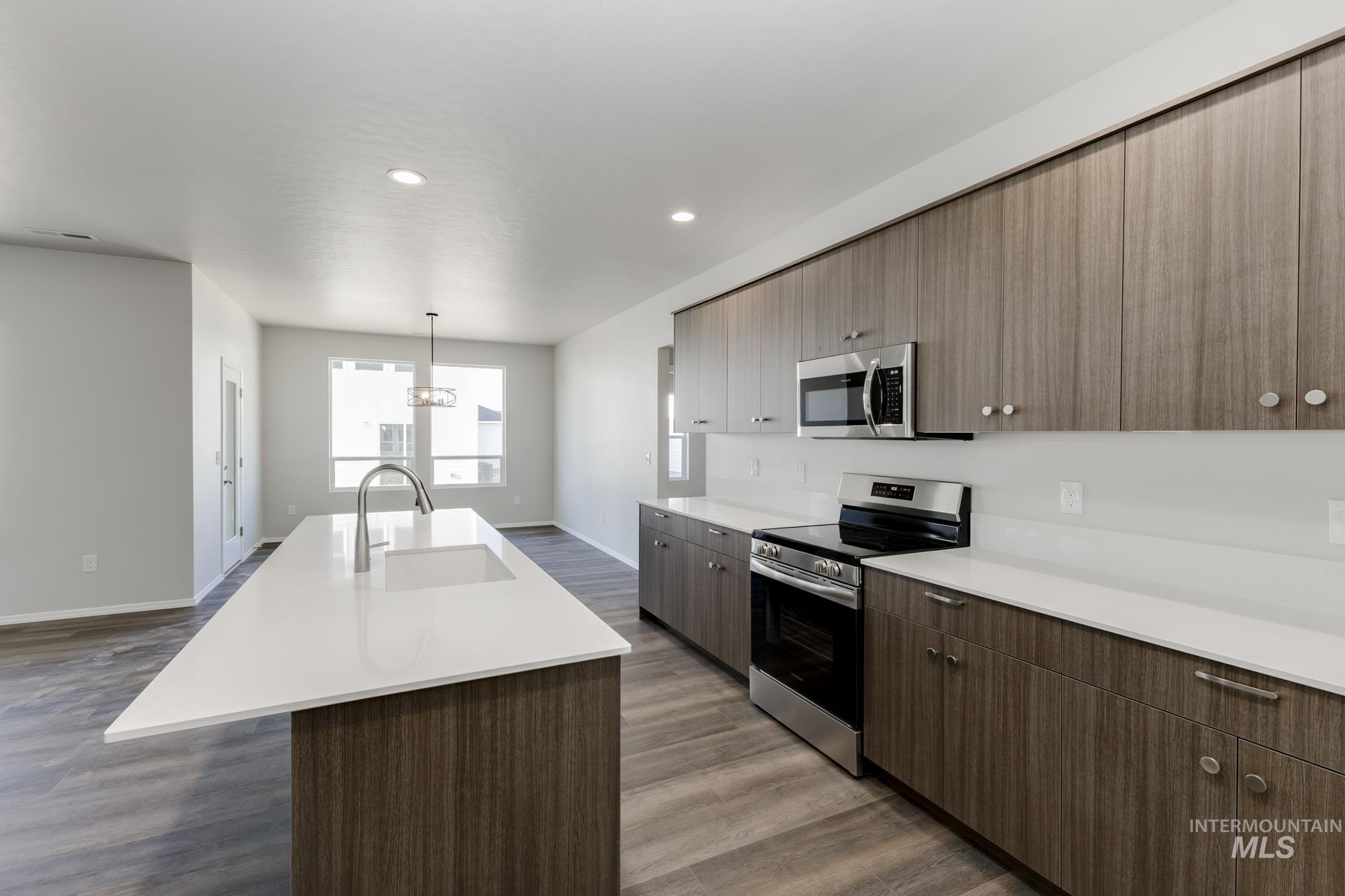 Kitchen with stainless steel appliances, a kitchen island with sink, light countertops, dark wood-type flooring, and recessed lighting