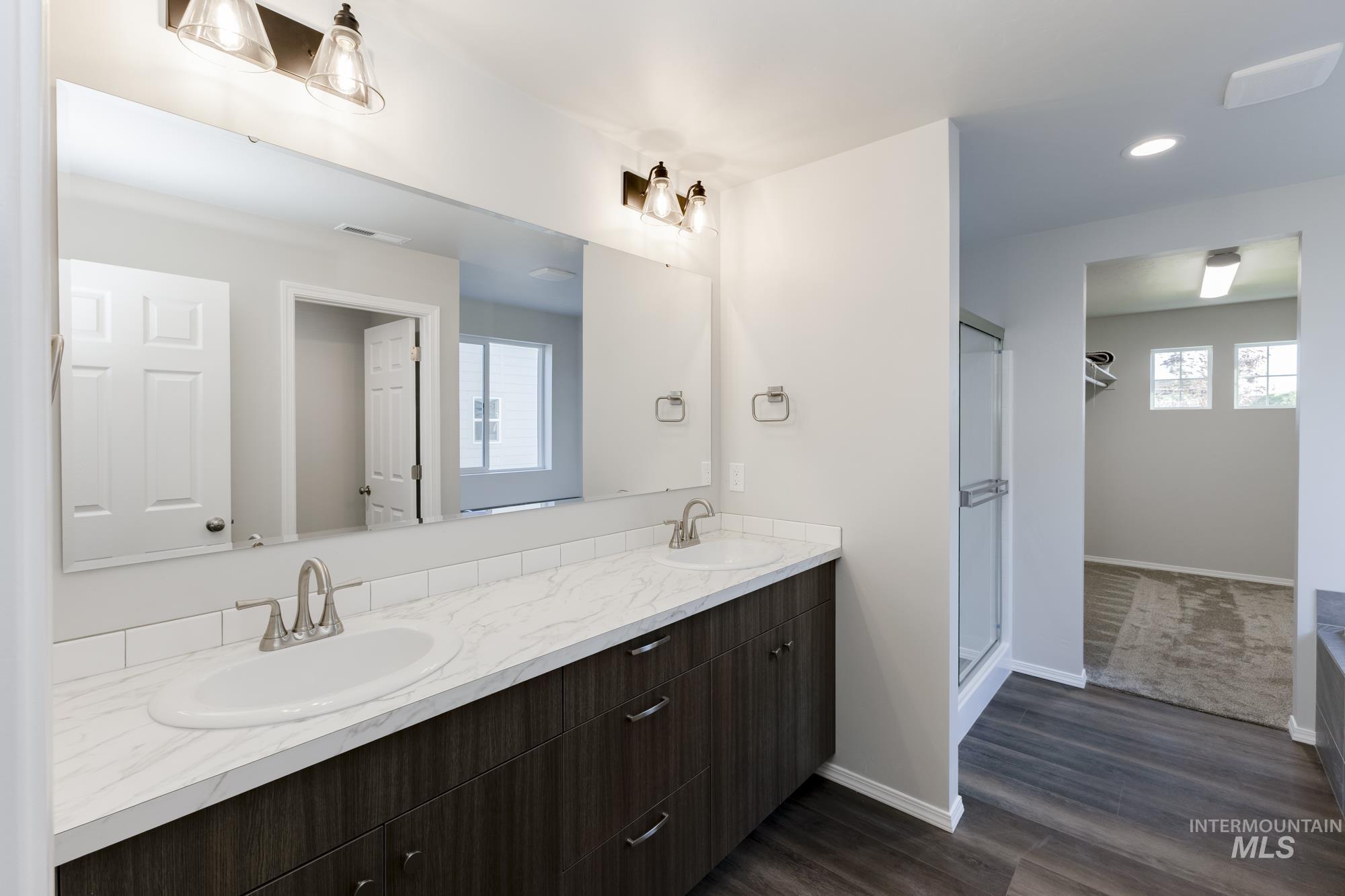 Bathroom with double vanity, a shower stall, wood finished floors, and recessed lighting