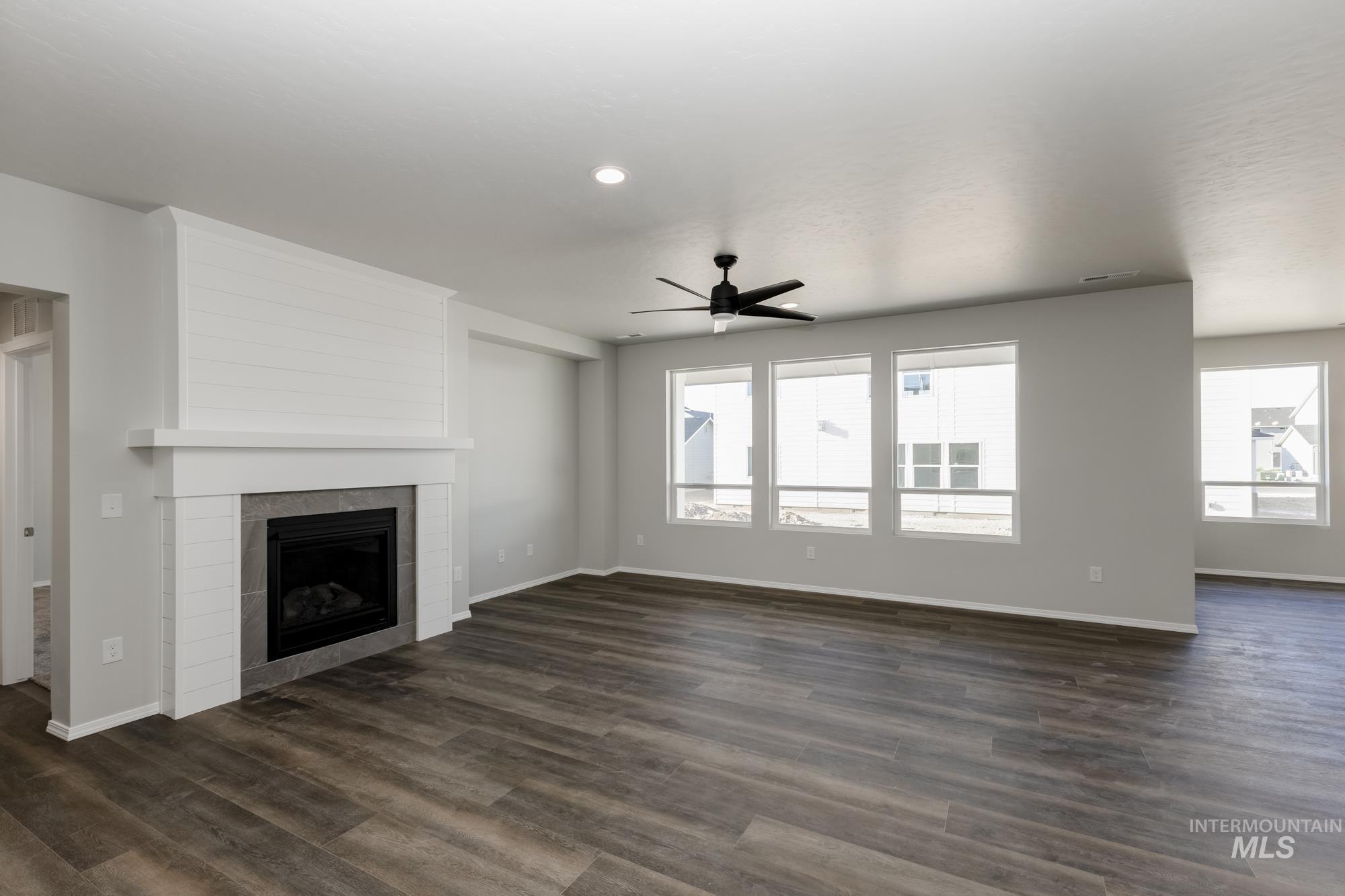 Unfurnished living room featuring healthy amount of natural light, a ceiling fan, dark wood-type flooring, a tile fireplace, and recessed lighting