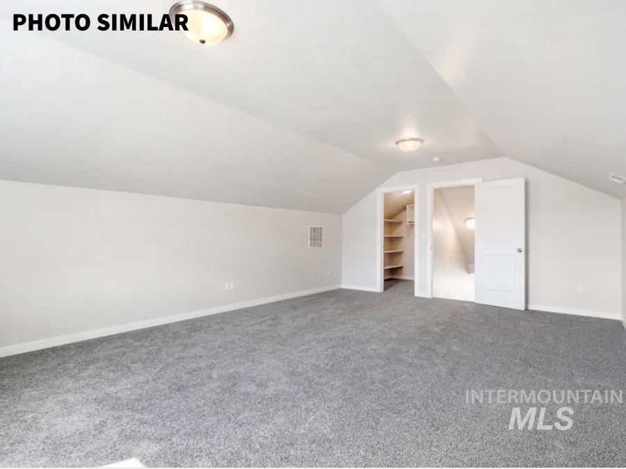Spacious room featuring sloped ceilings, plush gray carpeting, recessed doors, interior shelving, and flush-mount lighting fixtures