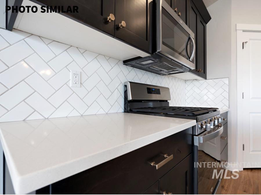 Kitchen featuring white herringbone pattern tile backsplash, white countertop, dark wood-finish cabinetry with gold-tone hardware, stainless steel range, and an over-the-range stainless steel microwave