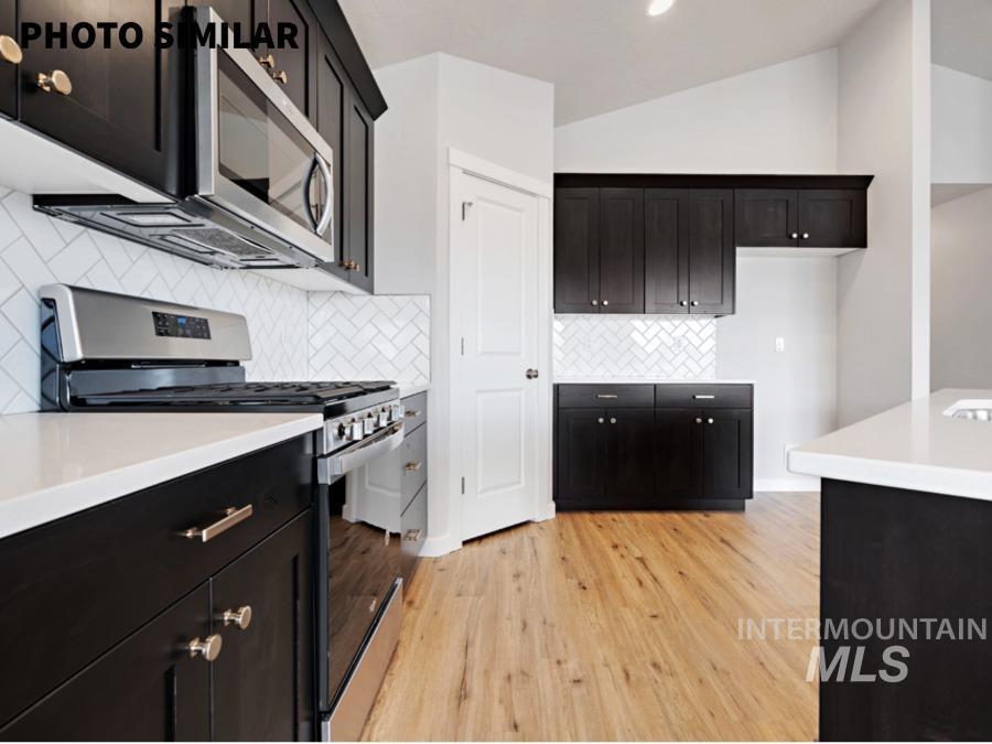 Kitchen featuring dark wood-finish cabinetry with brushed nickel hardware, white countertops, stainless steel appliances, a white herringbone tile backsplash, and light wood-finish flooring