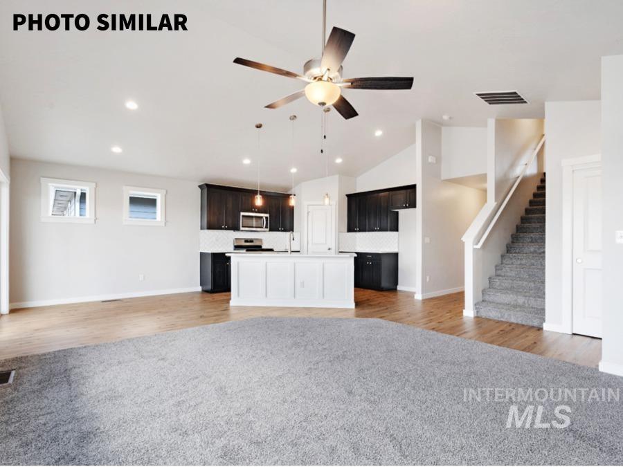 Open-concept living space featuring a kitchen island with paneling, dark wood-finish cabinetry, stainless steel appliances, and a tiled backsplash