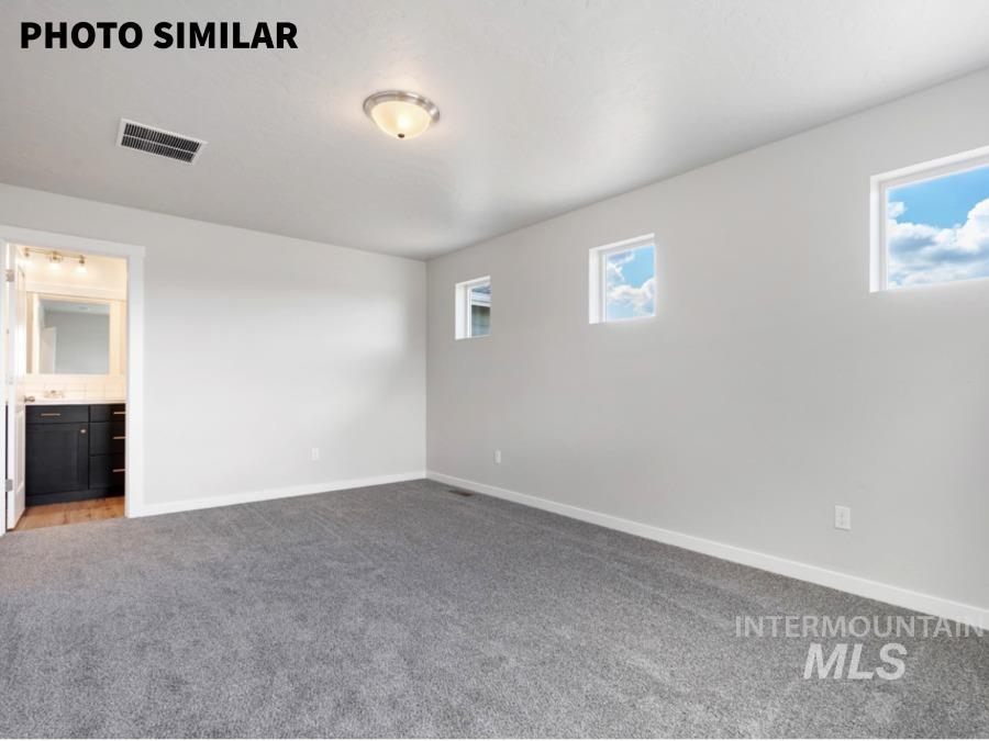 Spacious room featuring gray carpeting, white walls, two square windows, a flush-mount ceiling light fixture, and an attached bathroom with a dark wood-finish vanity and light-colored countertop