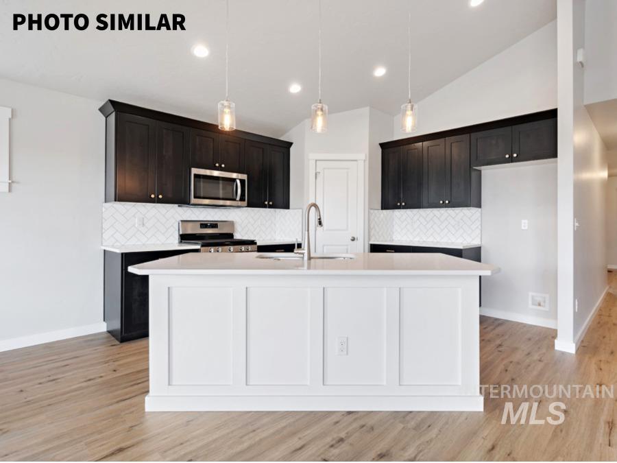 Spacious kitchen with a central island featuring paneling, dark wood-finish cabinetry, stainless steel appliances, a white herringbone tile backsplash, and wood-finish flooring