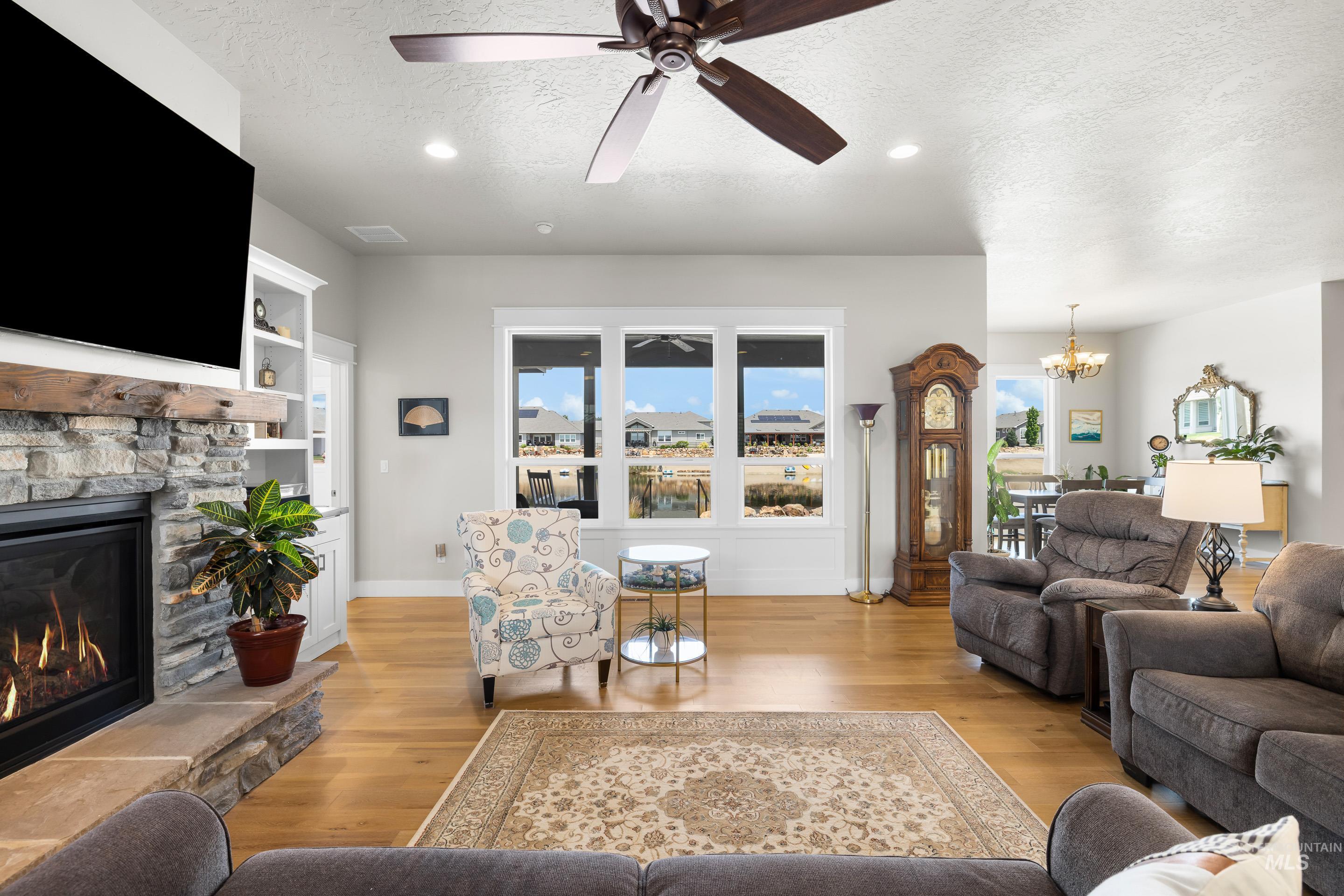 Living room featuring a textured ceiling, light wood finished floors, a fireplace, a chandelier, and ceiling fan