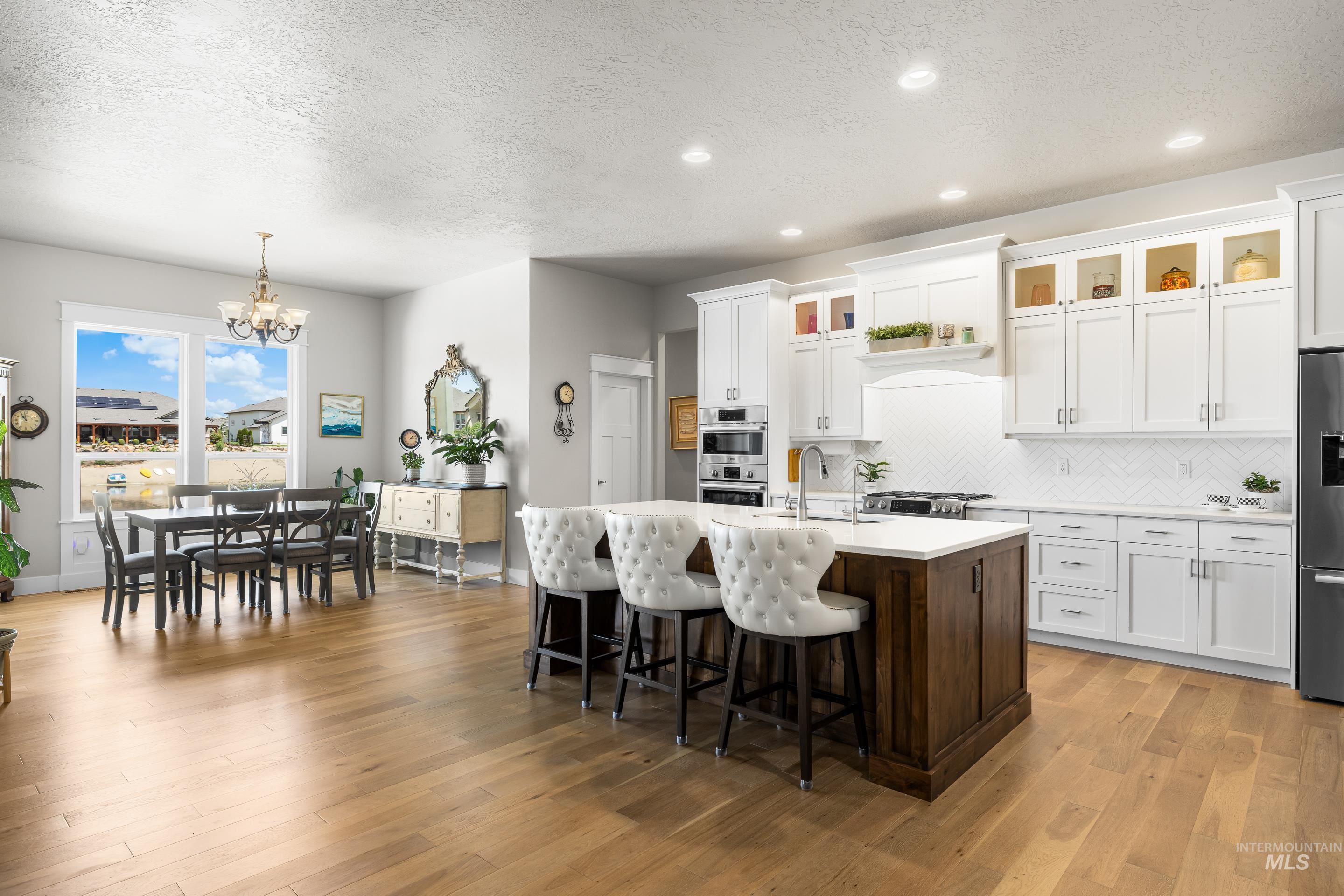 Kitchen featuring stainless steel appliances, a chandelier, a textured ceiling, light countertops, and an island with sink