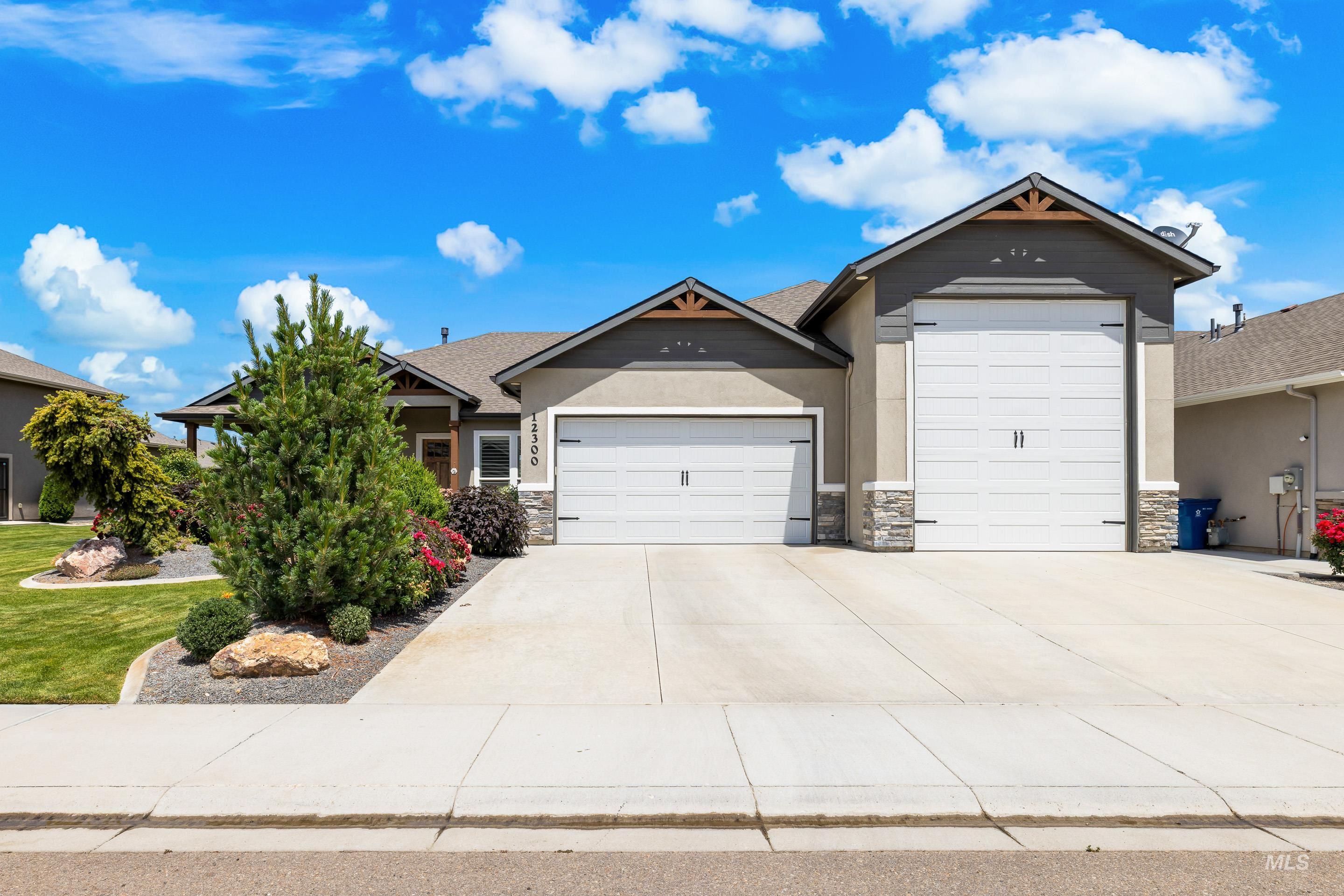 View of front of home with an attached garage, stone siding, driveway, stucco siding, and a front lawn