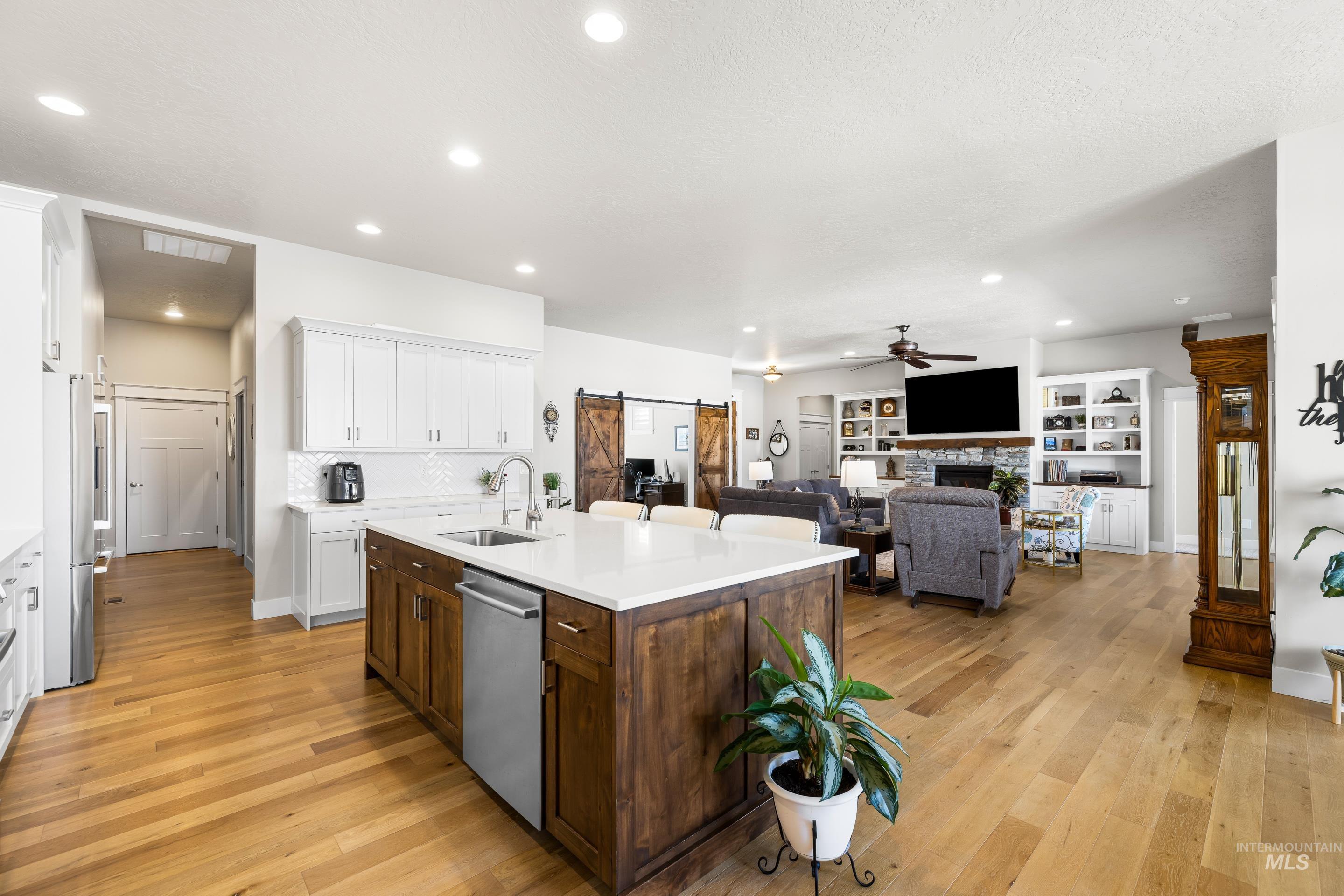 Kitchen with stainless steel appliances, a ceiling fan, a barn door, a kitchen island with sink, and white cabinets