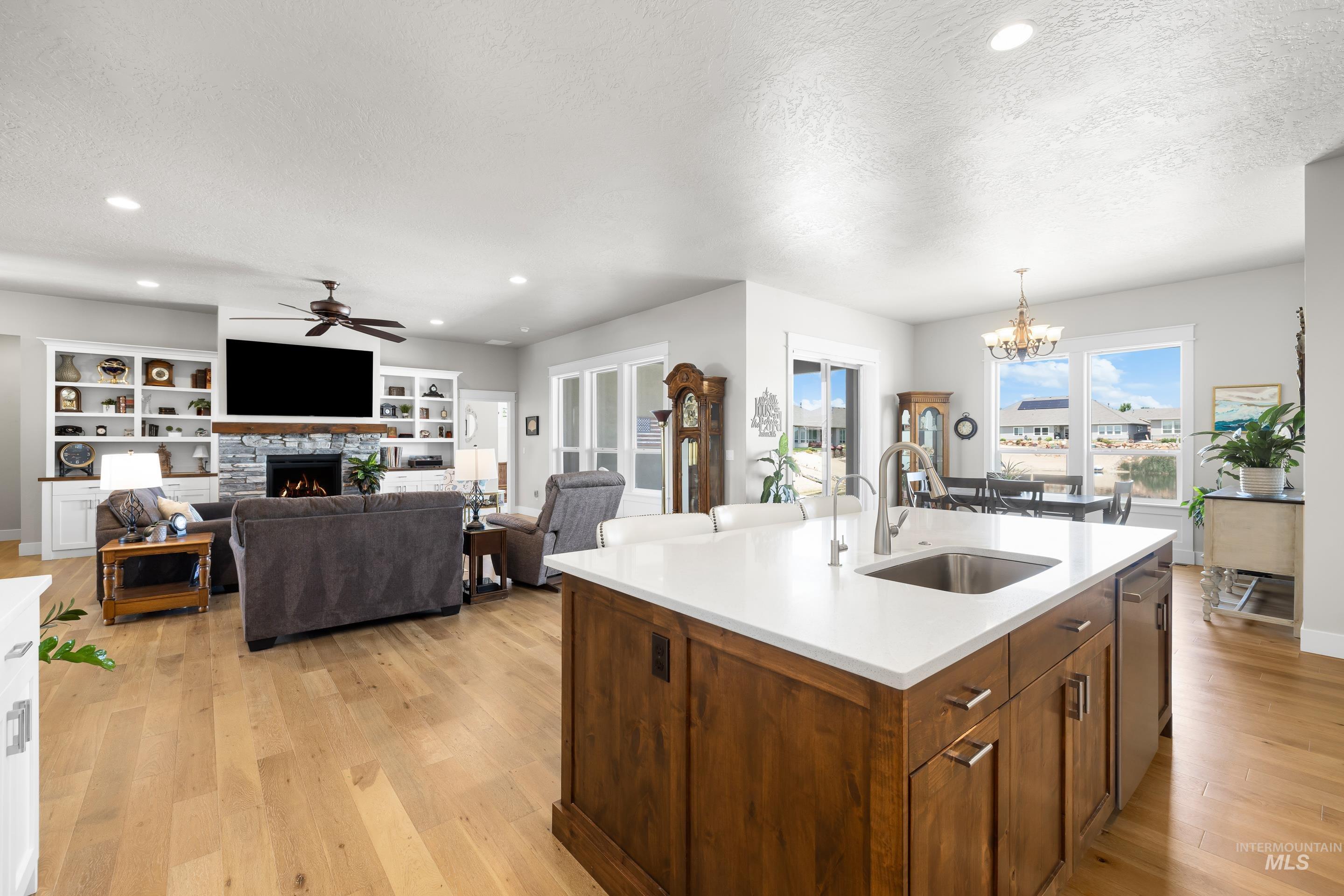 Kitchen featuring ceiling fan, a fireplace, light wood finished floors, light countertops, and a textured ceiling