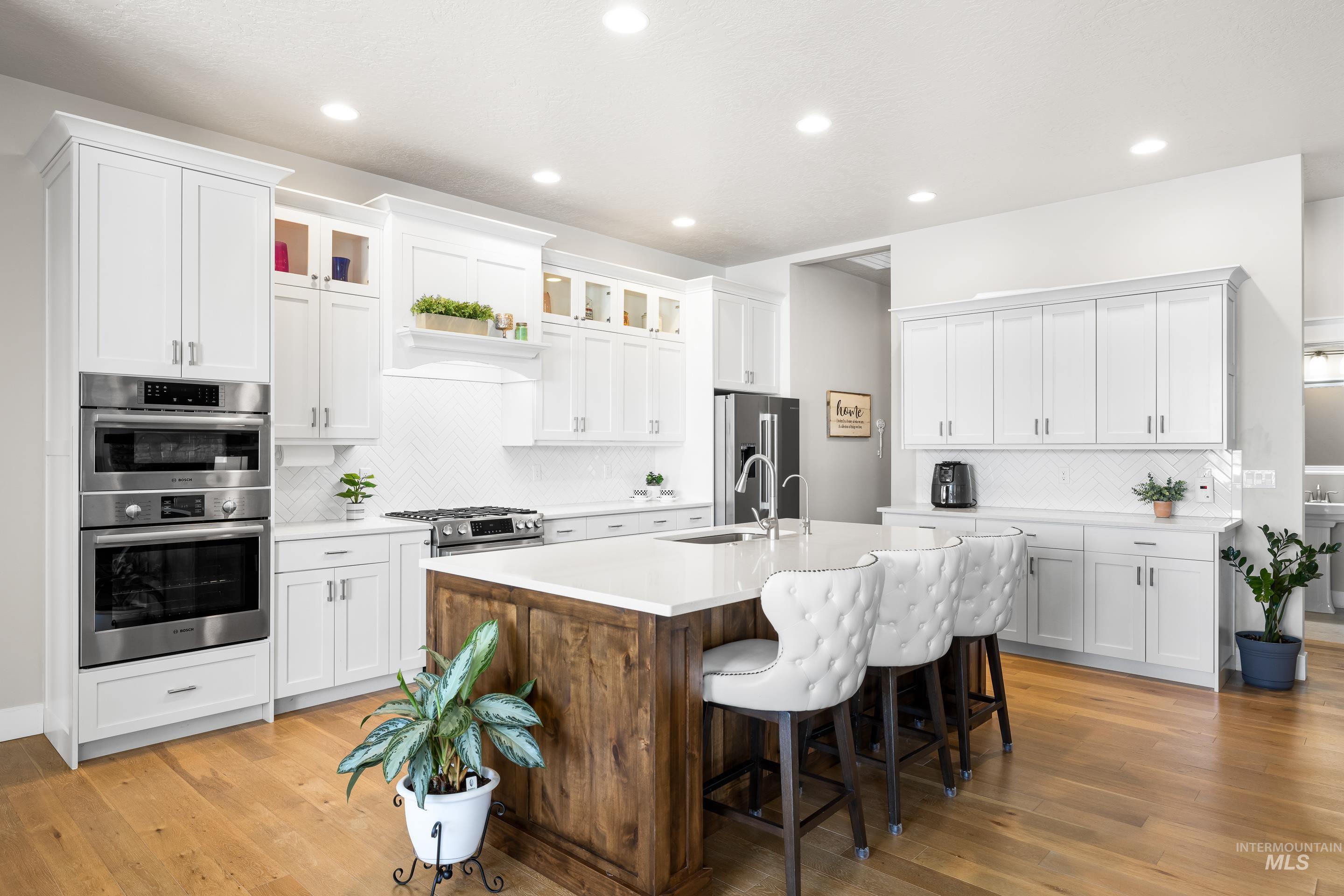Kitchen with appliances with stainless steel finishes, backsplash, a breakfast bar, light countertops, and a kitchen island with sink