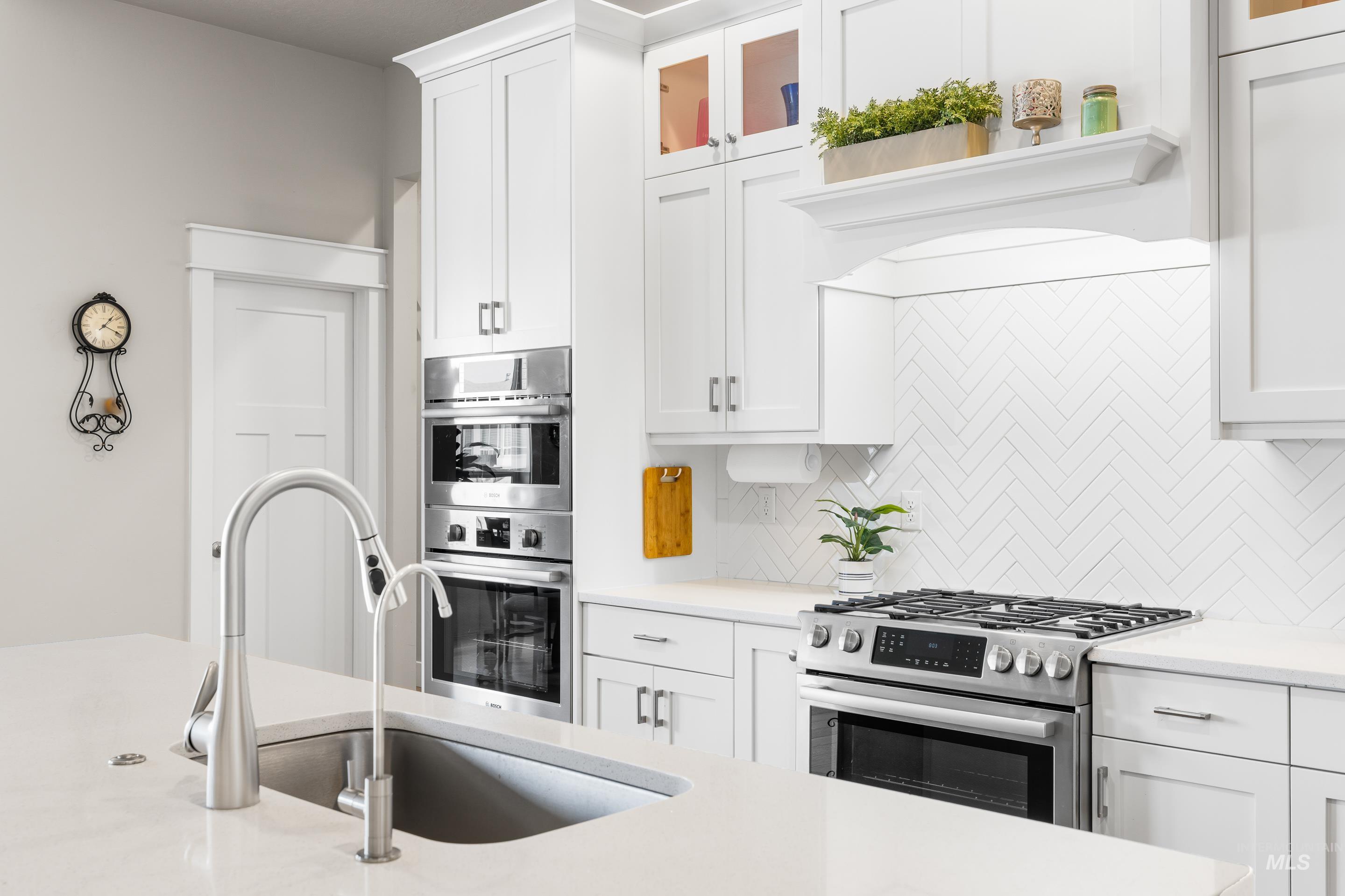 Kitchen featuring stainless steel appliances, decorative backsplash, light countertops, and white cabinetry