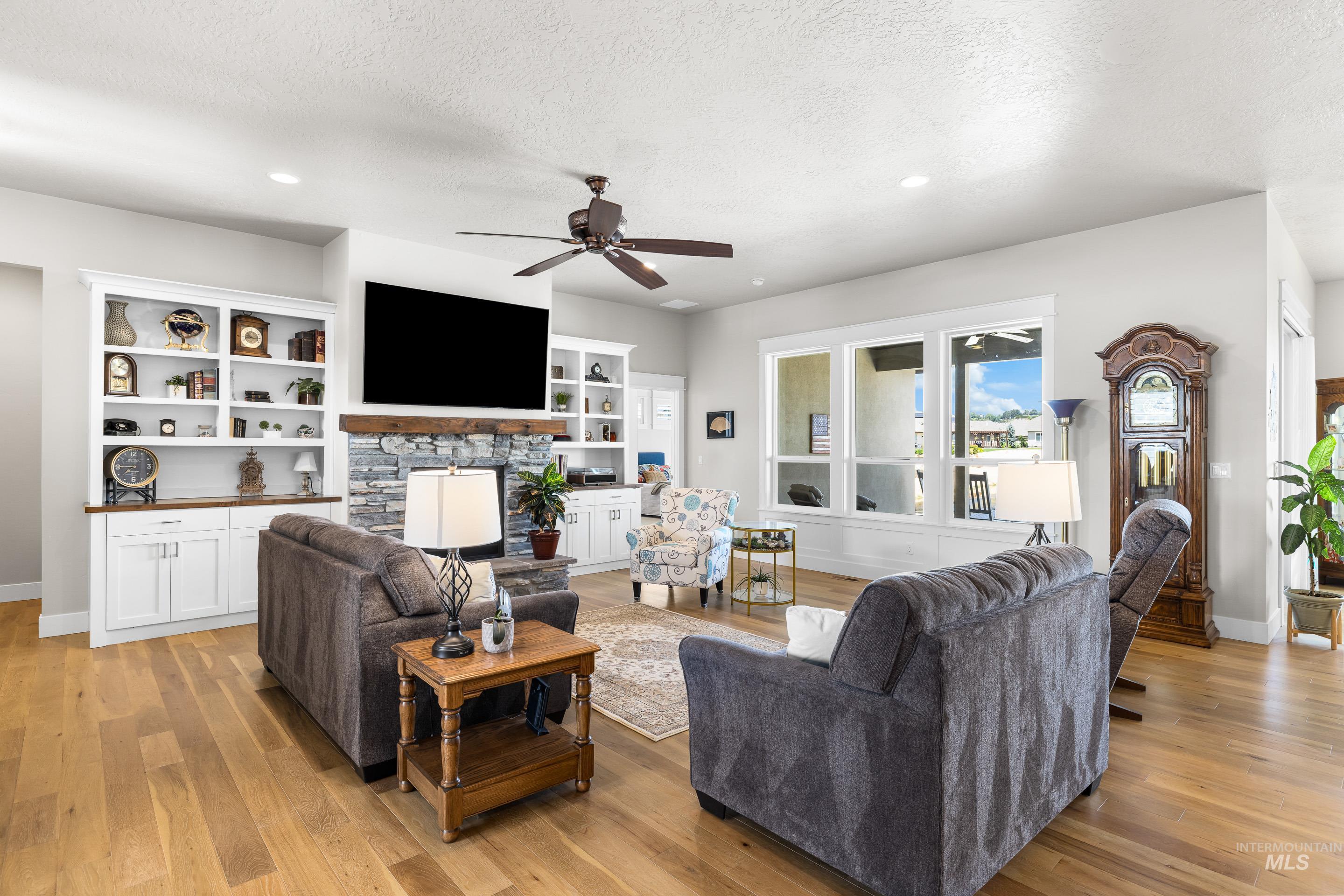 Living room with a textured ceiling, a ceiling fan, light wood-style floors, a fireplace, and recessed lighting