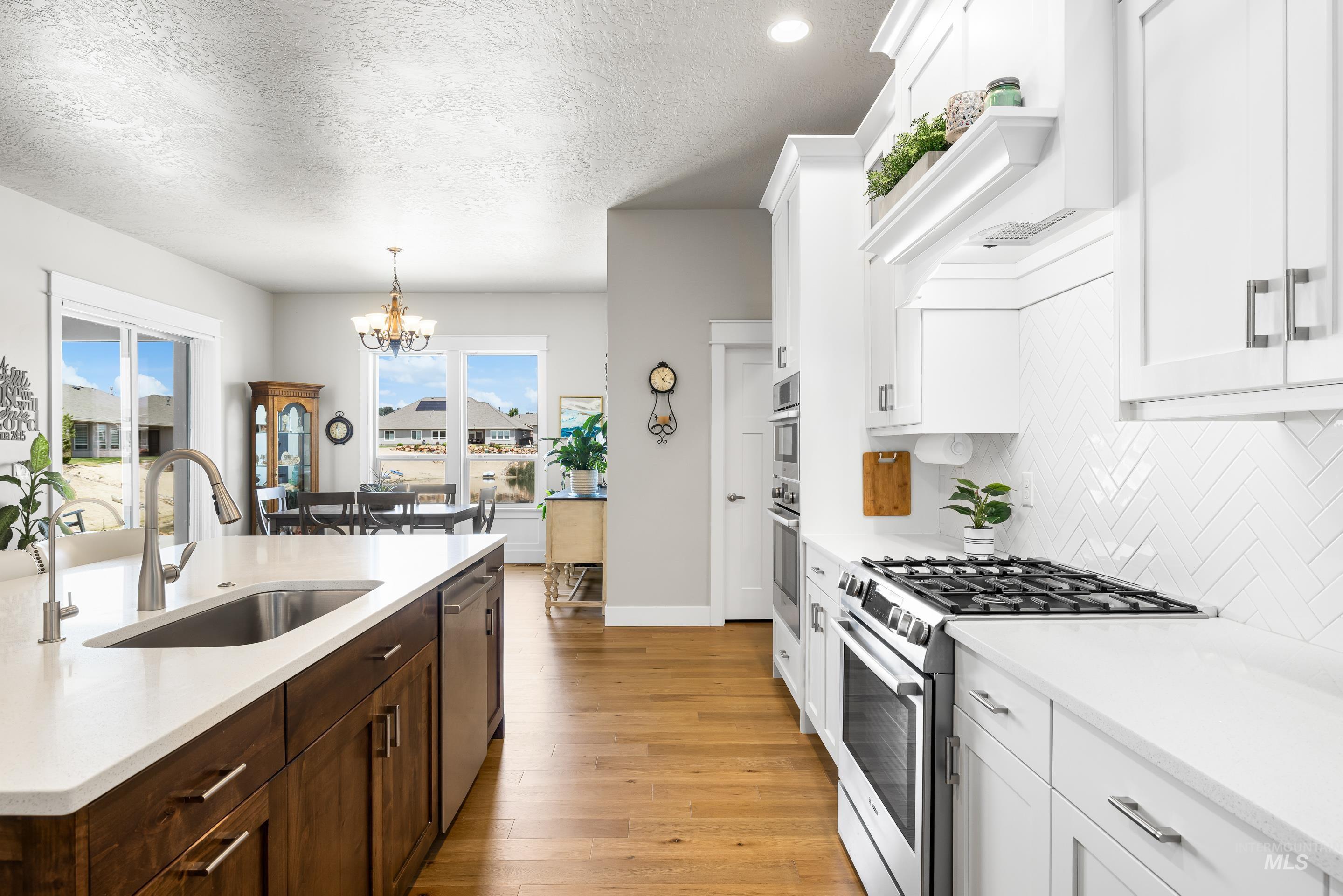 Kitchen featuring stainless steel appliances, a chandelier, light countertops, light wood-type flooring, and a textured ceiling