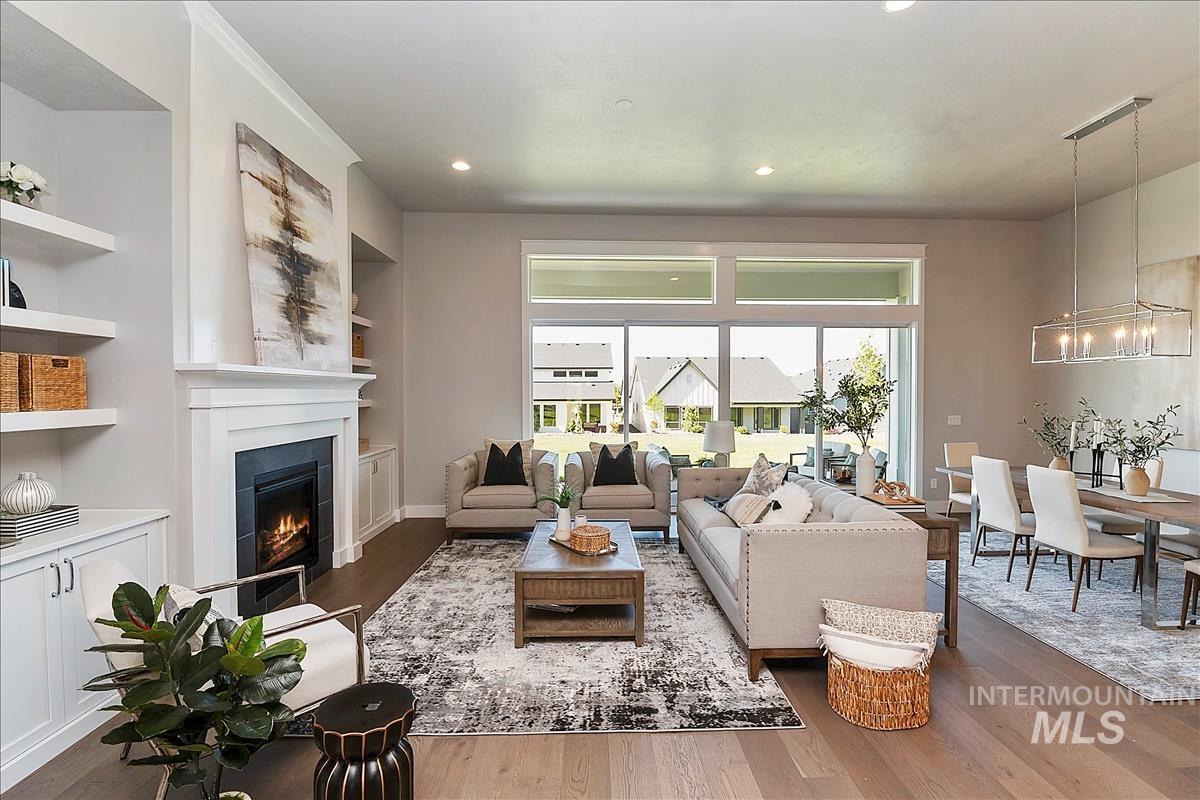 Living area with wood finished floors, built in shelves, a warm lit fireplace, and recessed lighting