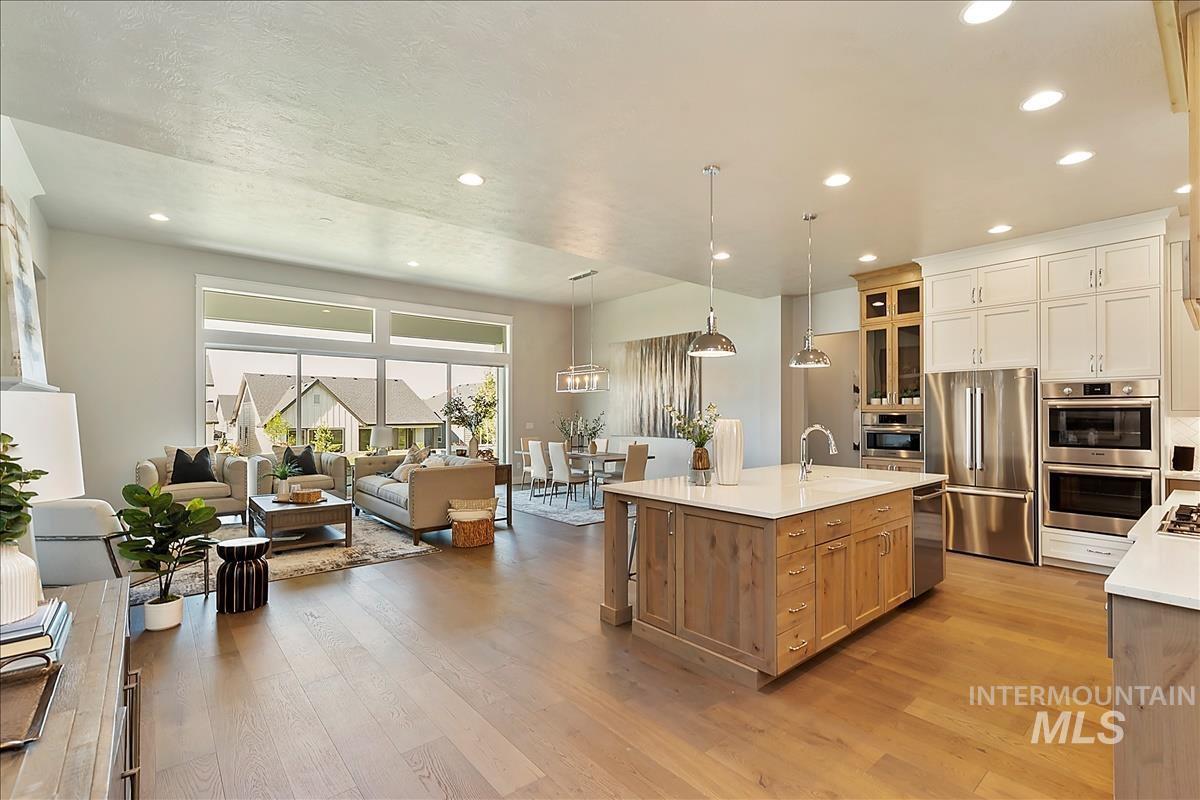 Kitchen with open floor plan, stainless steel appliances, hanging light fixtures, light stone countertops, and glass fronted cabinets
