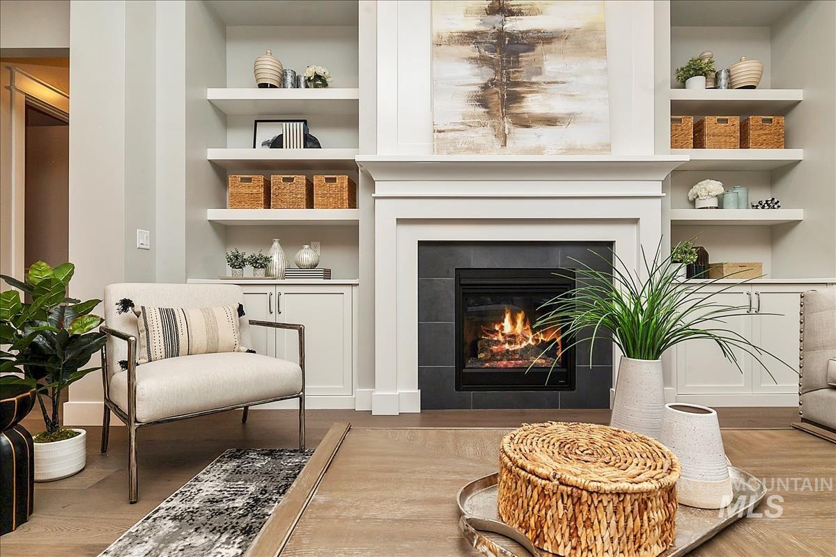 Living area with built in shelves, wood finished floors, and a tiled fireplace