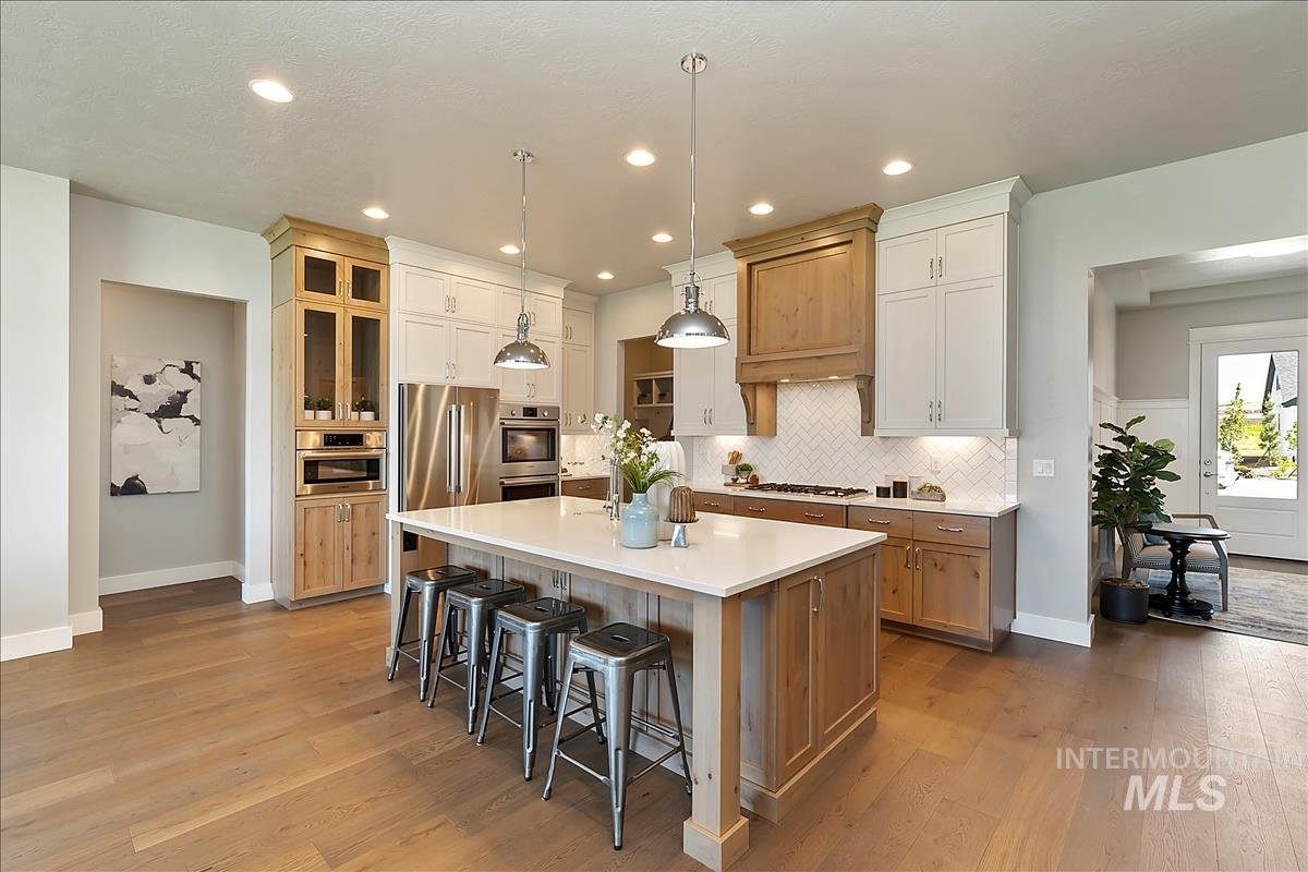 Dual tone kitchen with dual tone cabinetry, decorative light fixtures, a center island with sink, light wood-style flooring, and a kitchen breakfast bar