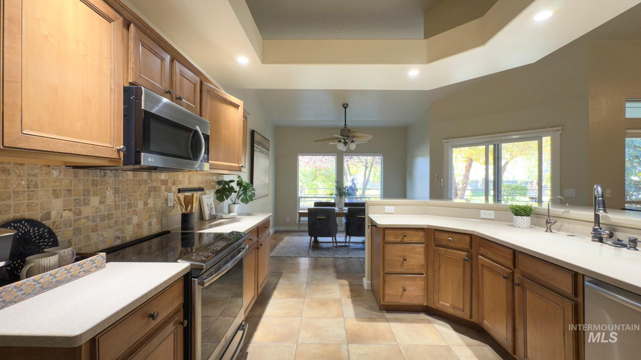 Kitchen with brown cabinetry, appliances with stainless steel finishes, recessed lighting, a tray ceiling, and decorative backsplash