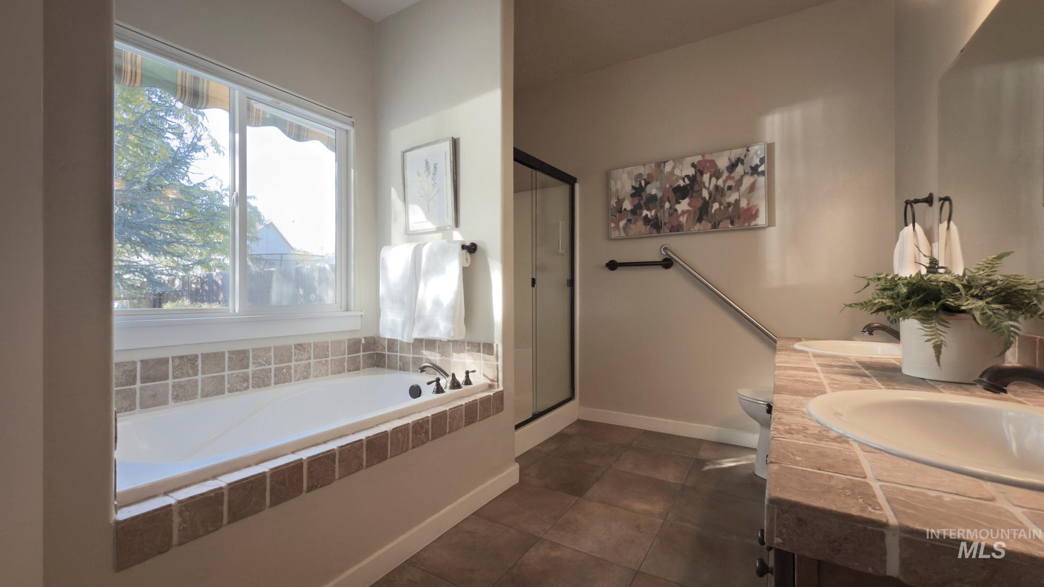Bathroom featuring a stall shower, a bath, double vanity, and dark tile patterned floors